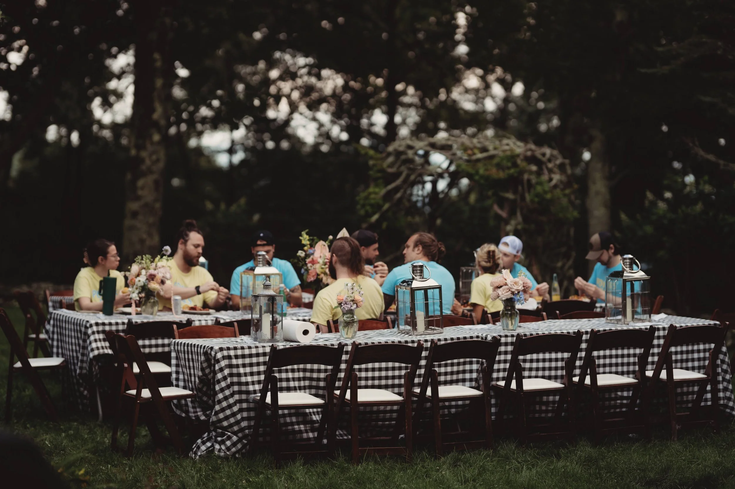 Outdoor rehearsal dinner with a long table, black-and-white gingham tablecloths, and lantern centerpieces
