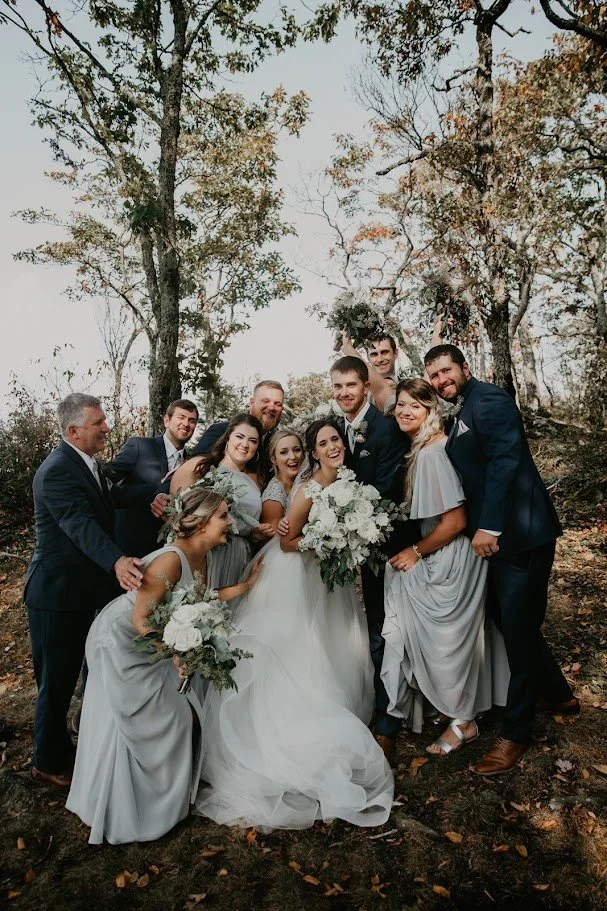 Bride and groom surrounded by bridesmaids and groomsmen for a joyful woodland wedding party portrait.