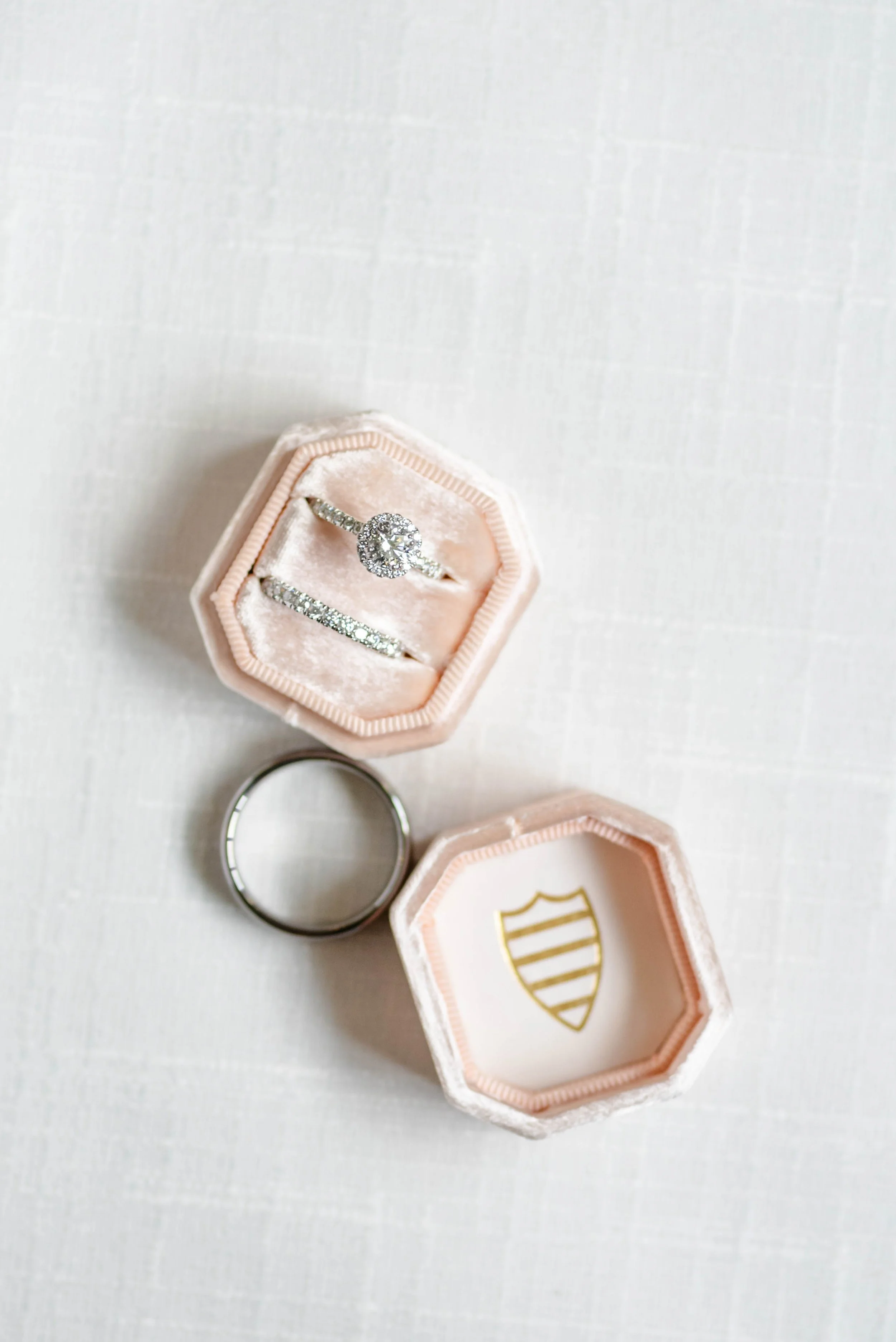 Wedding rings displayed in blush velvet ring boxes on a soft white surface.
