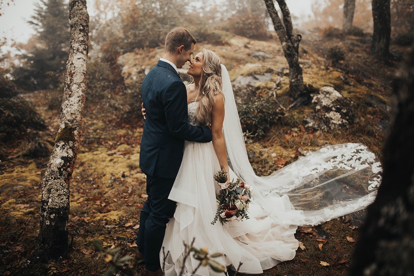 Bride and groom kissing in the woods with the veil and dress train flowing behind them.