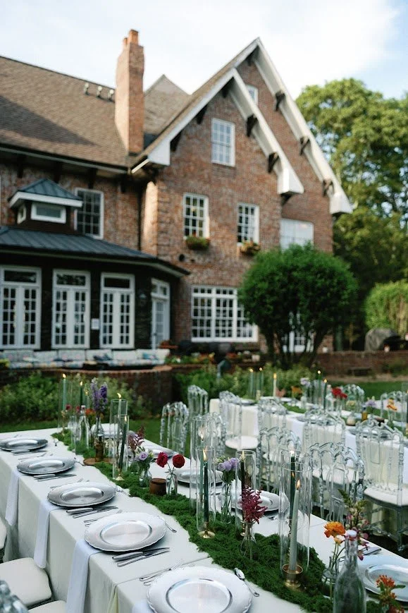 Outdoor wedding reception table setup with florals in front of a brick estate.