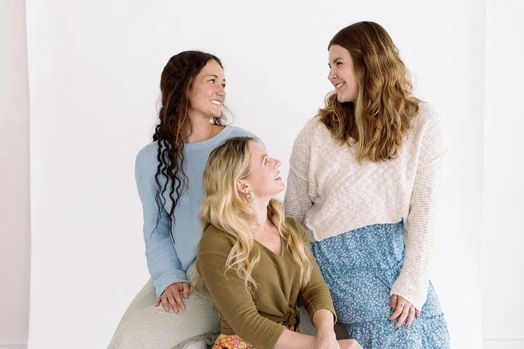 Three women smiling and looking at each other during a relaxed studio lifestyle portrait.