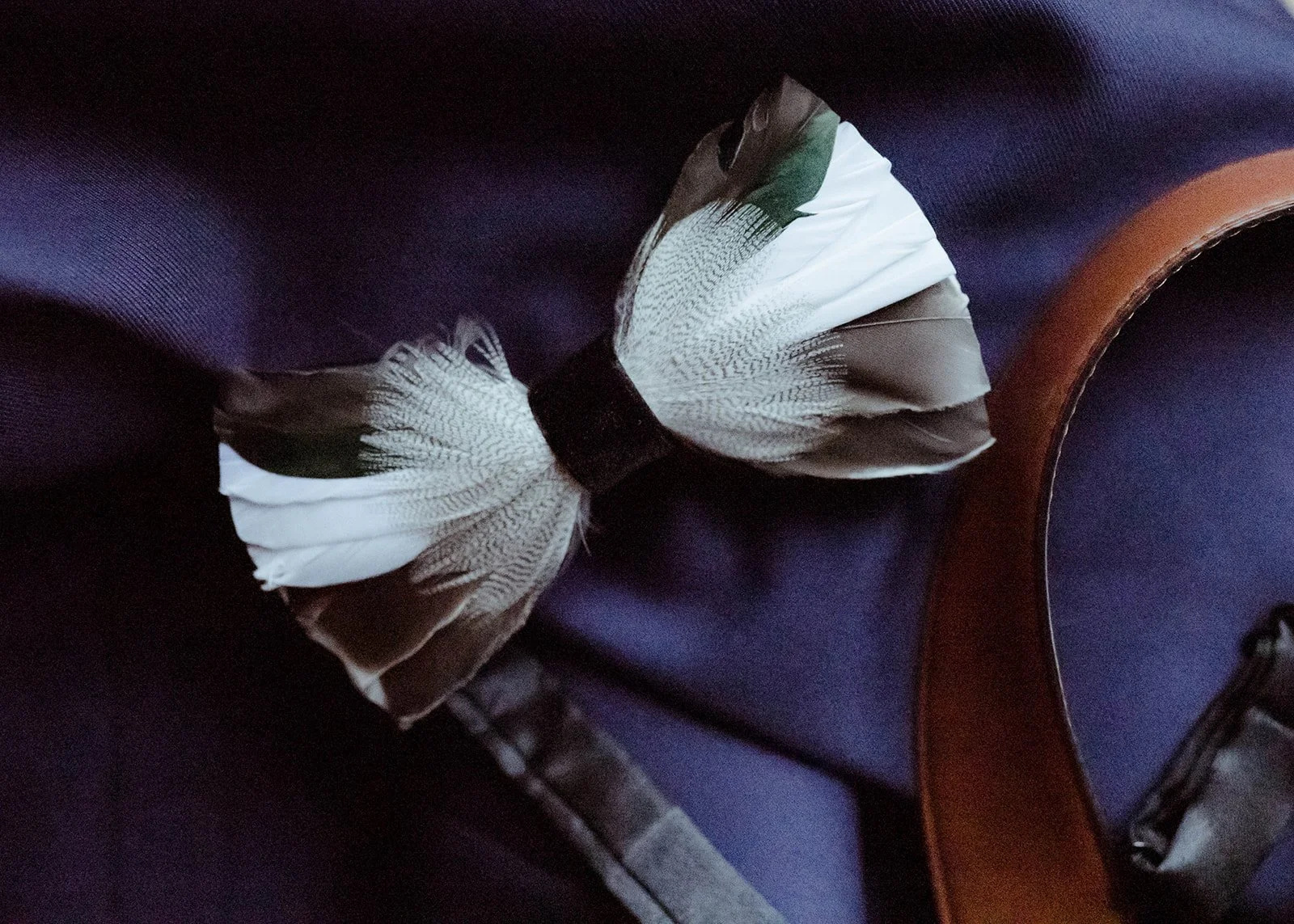 Close-up of a feather bow tie and leather suspenders as groom detail accessories