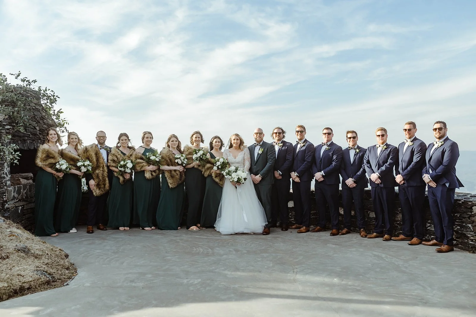 Bride and groom posing with their full wedding party at a scenic mountain overlook ceremony location.