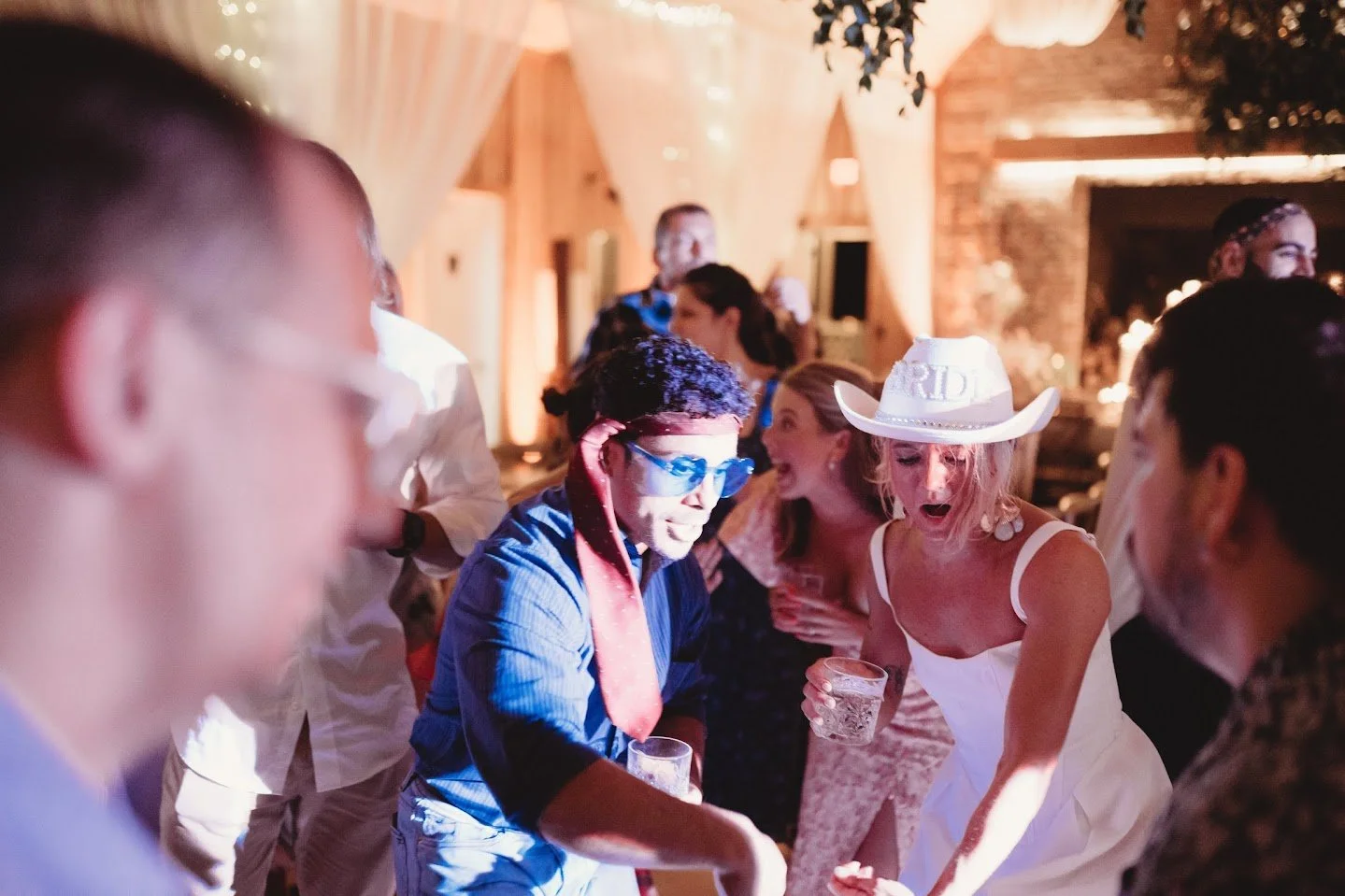 Wedding reception dance floor moment with the bride in a cowgirl hat and guests cheering.