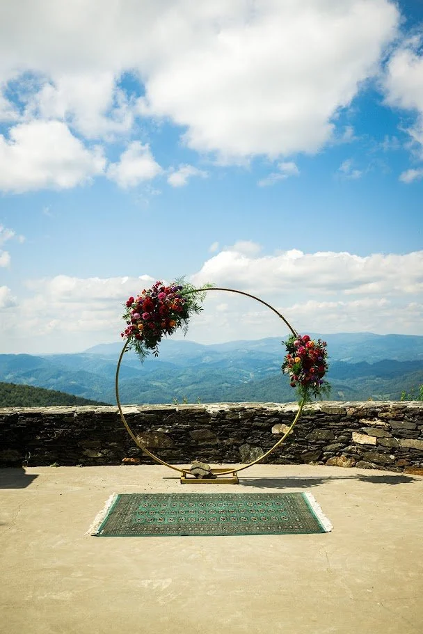 Circular wedding arch with colorful floral clusters on a mountain overlook ceremony terrace under a blue sky