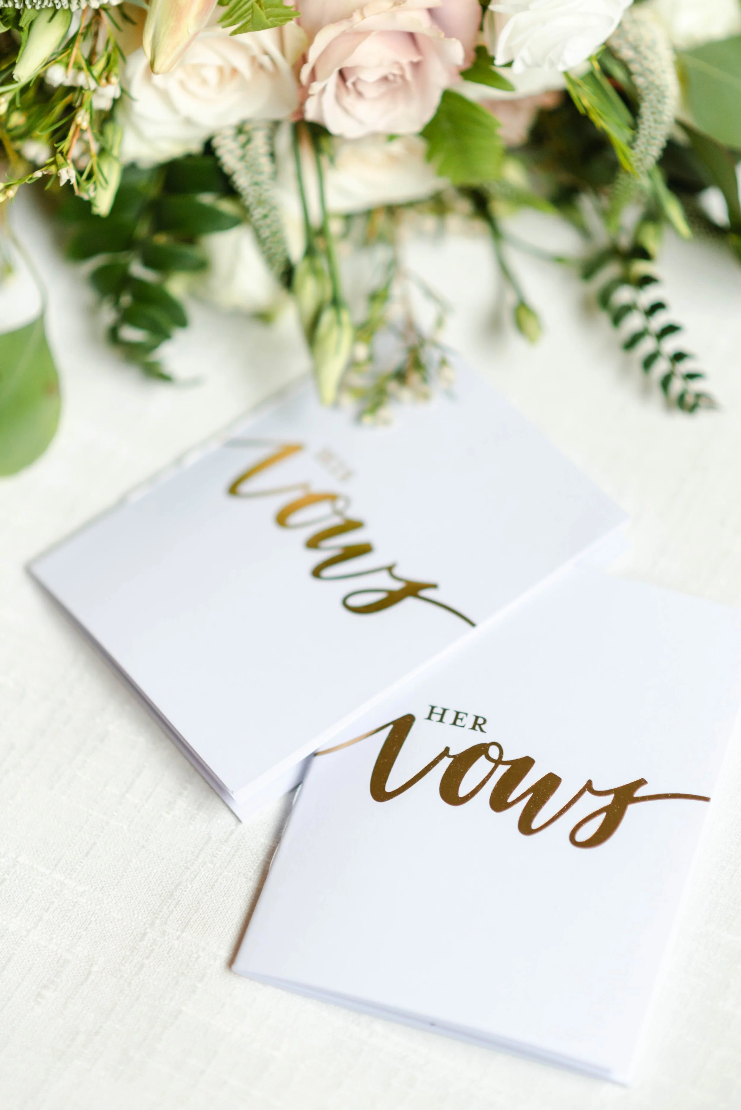 His and her wedding vow books photographed with a soft pink and white bridal bouquet.