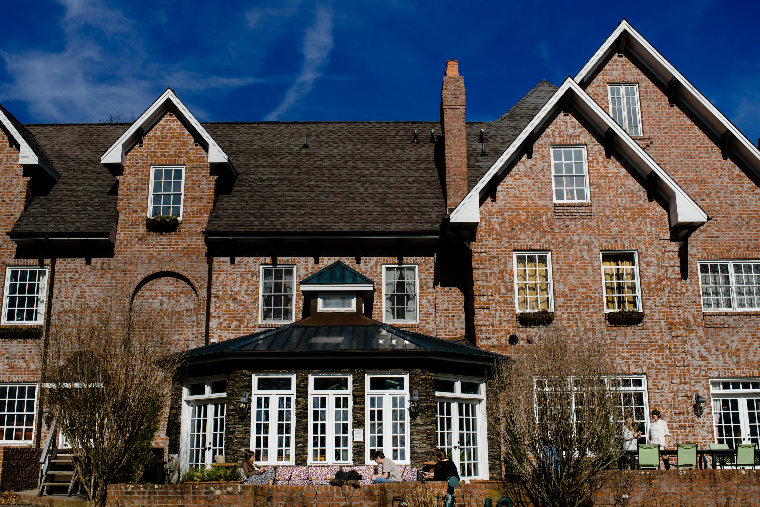 Brick wedding venue exterior with large windows and a stone patio under a blue sky.