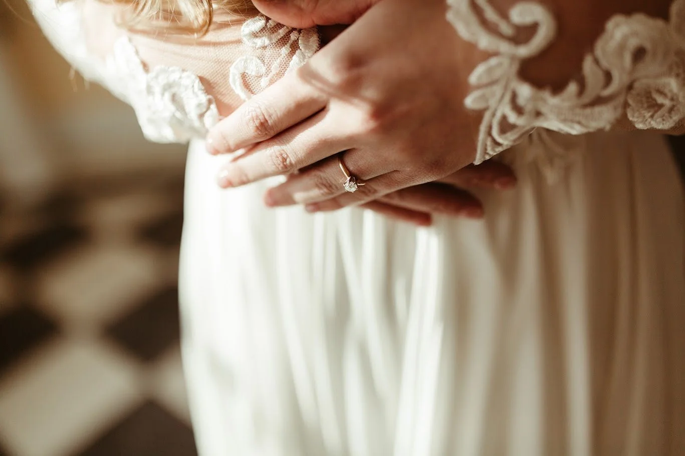 Close-up of the bride’s hands resting on the waist of her lace wedding dress.