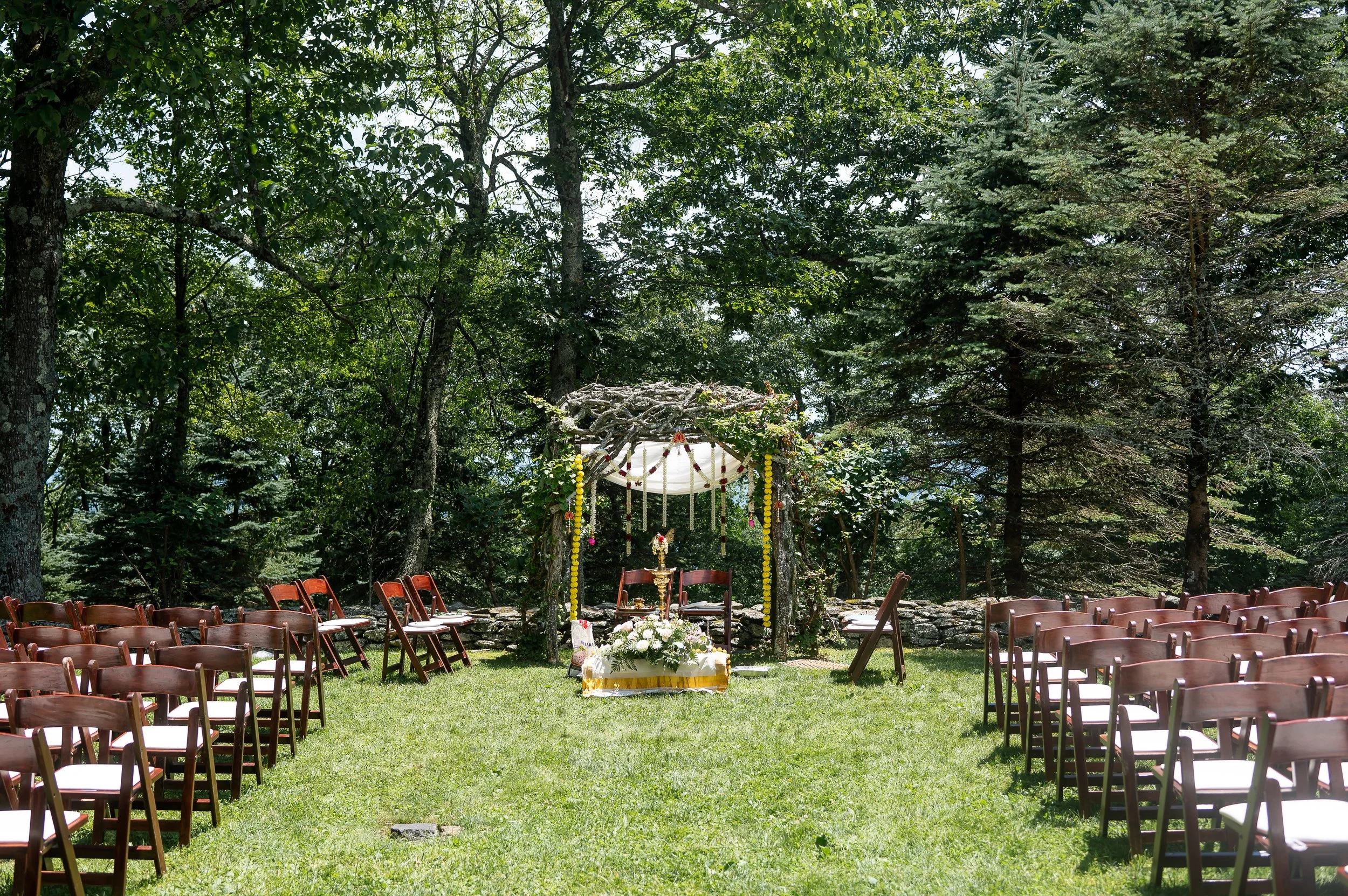 Outdoor Hindu wedding ceremony setup with chairs, floral mandap, and greenery in a garden setting.
