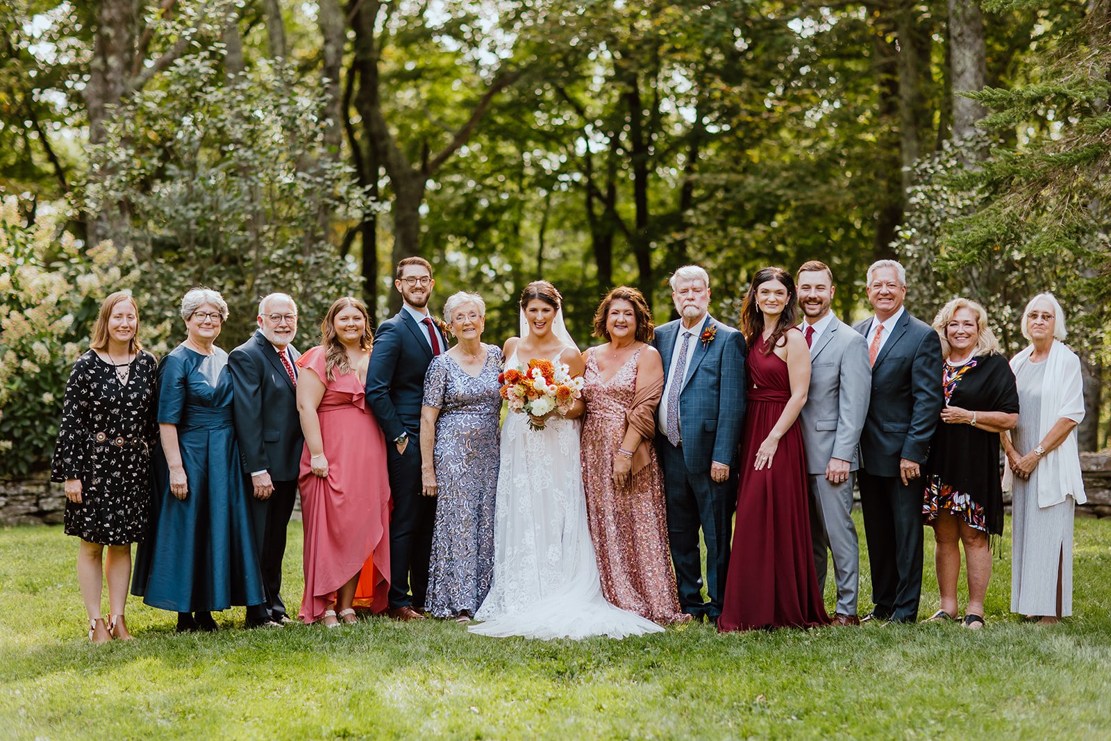 Bride and groom posing with family outdoors in a garden setting with warm autumn wedding florals.