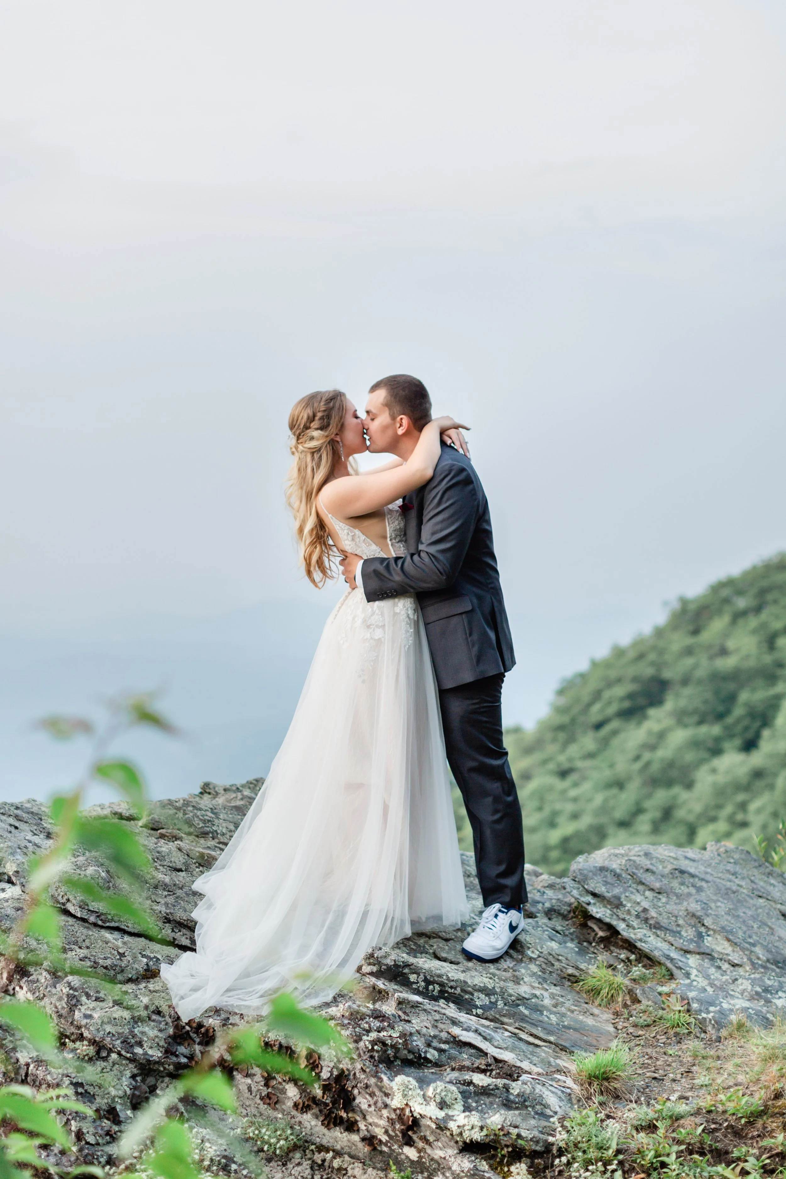 Bride and groom kissing on rocky terrain with mountains in the background.