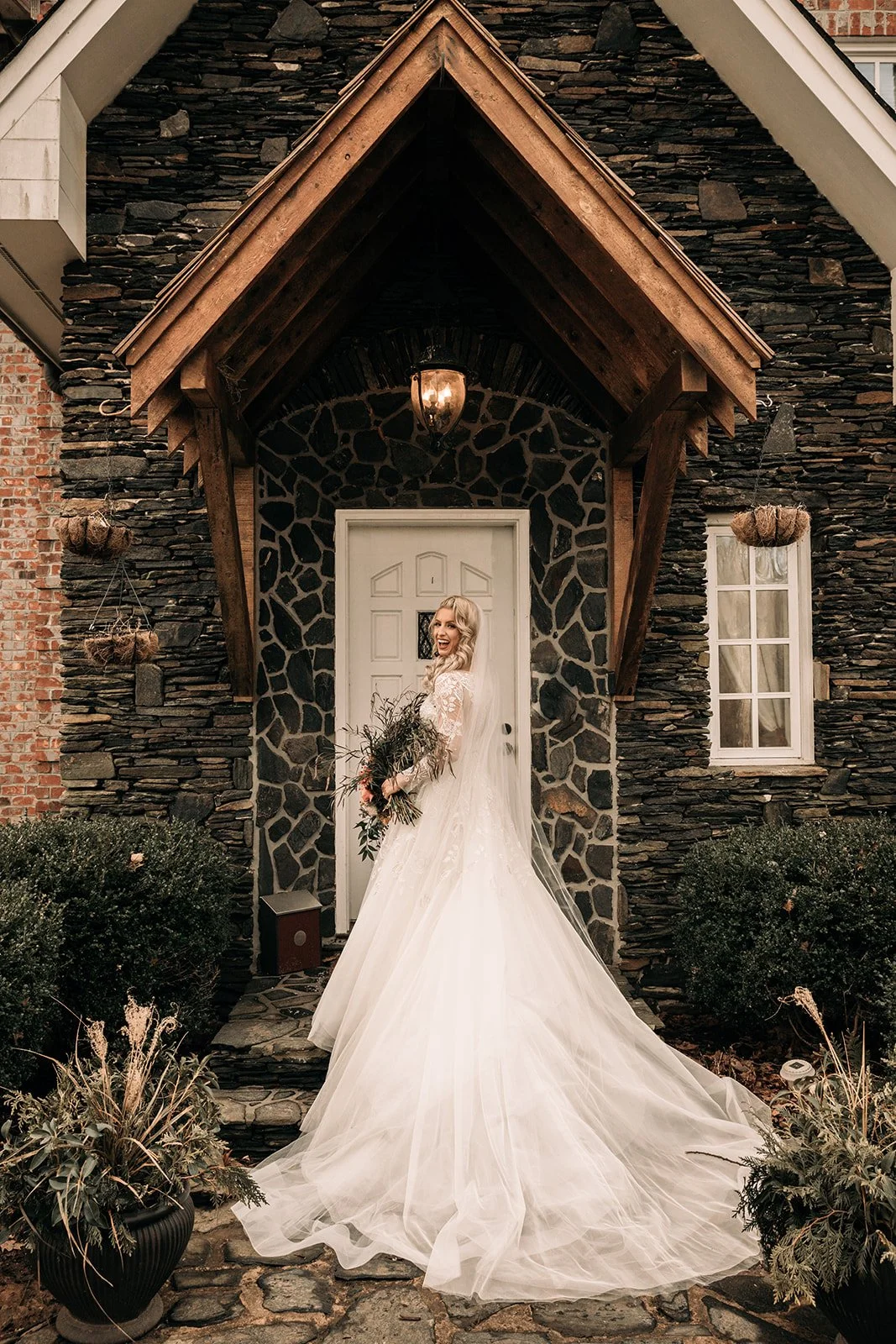Bride standing outside a stone cottage doorway in a flowing wedding dress with a dramatic train.