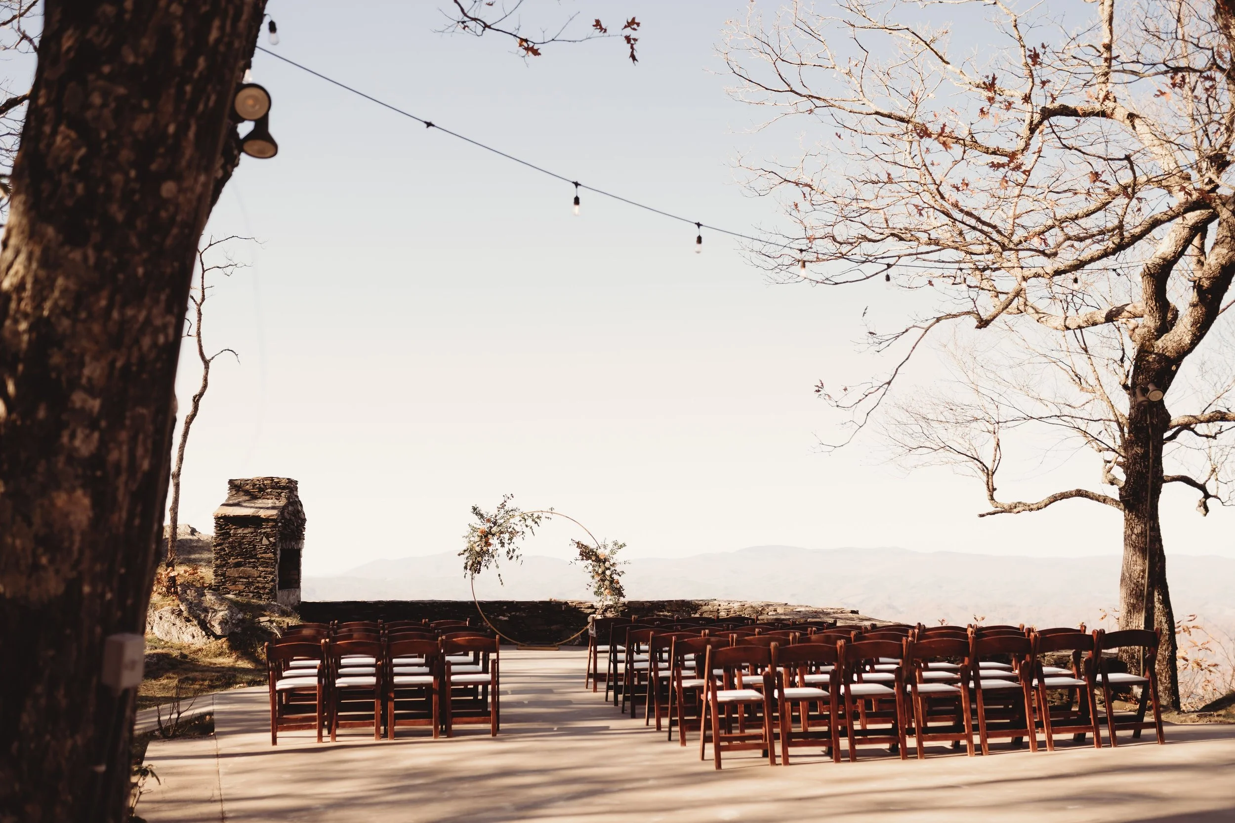 Outdoor mountain ceremony setup with rows of wooden chairs facing a scenic overlook