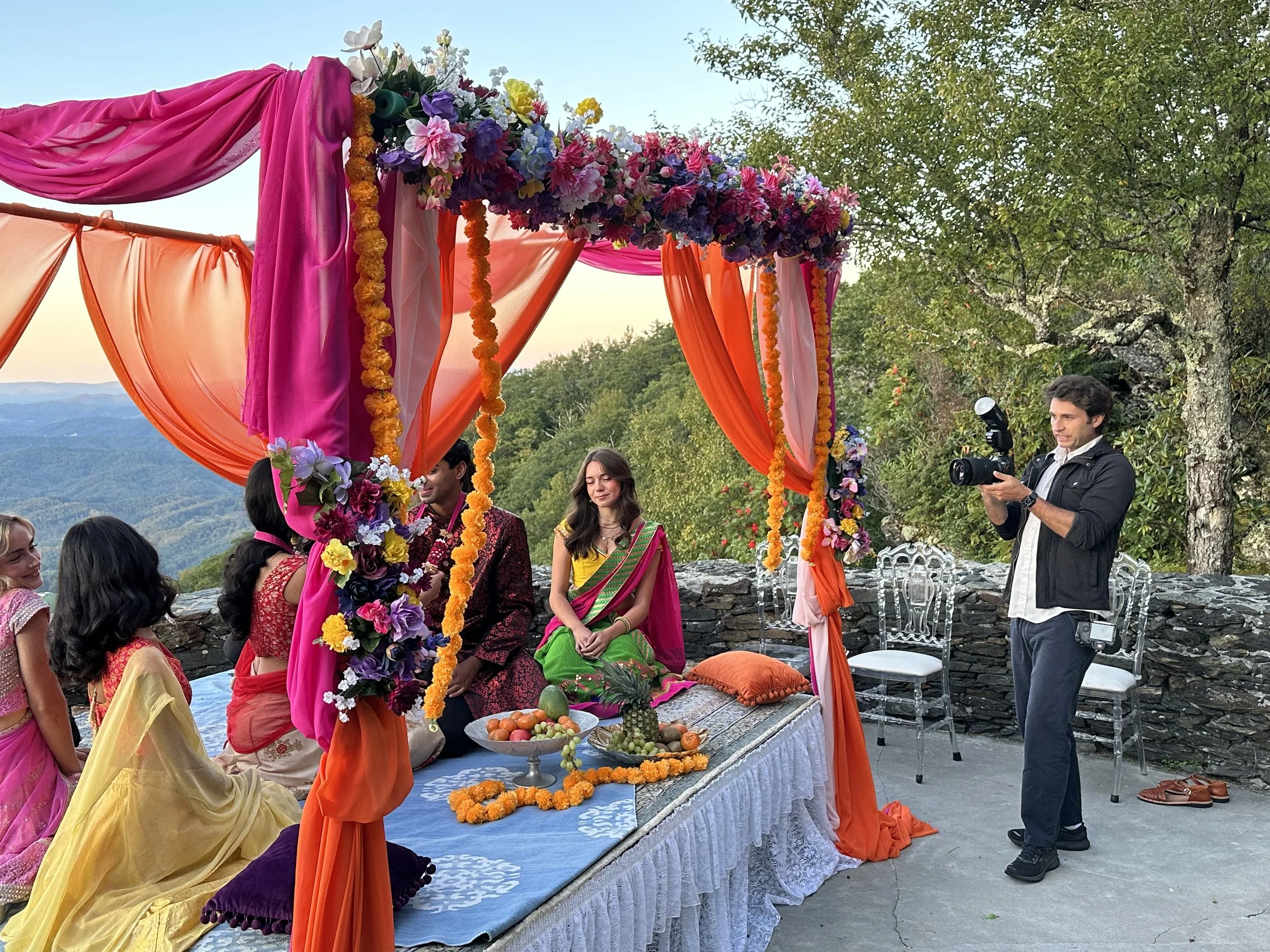 Videographer filming an Indian ceremony under a colorful mandap with a mountain view
