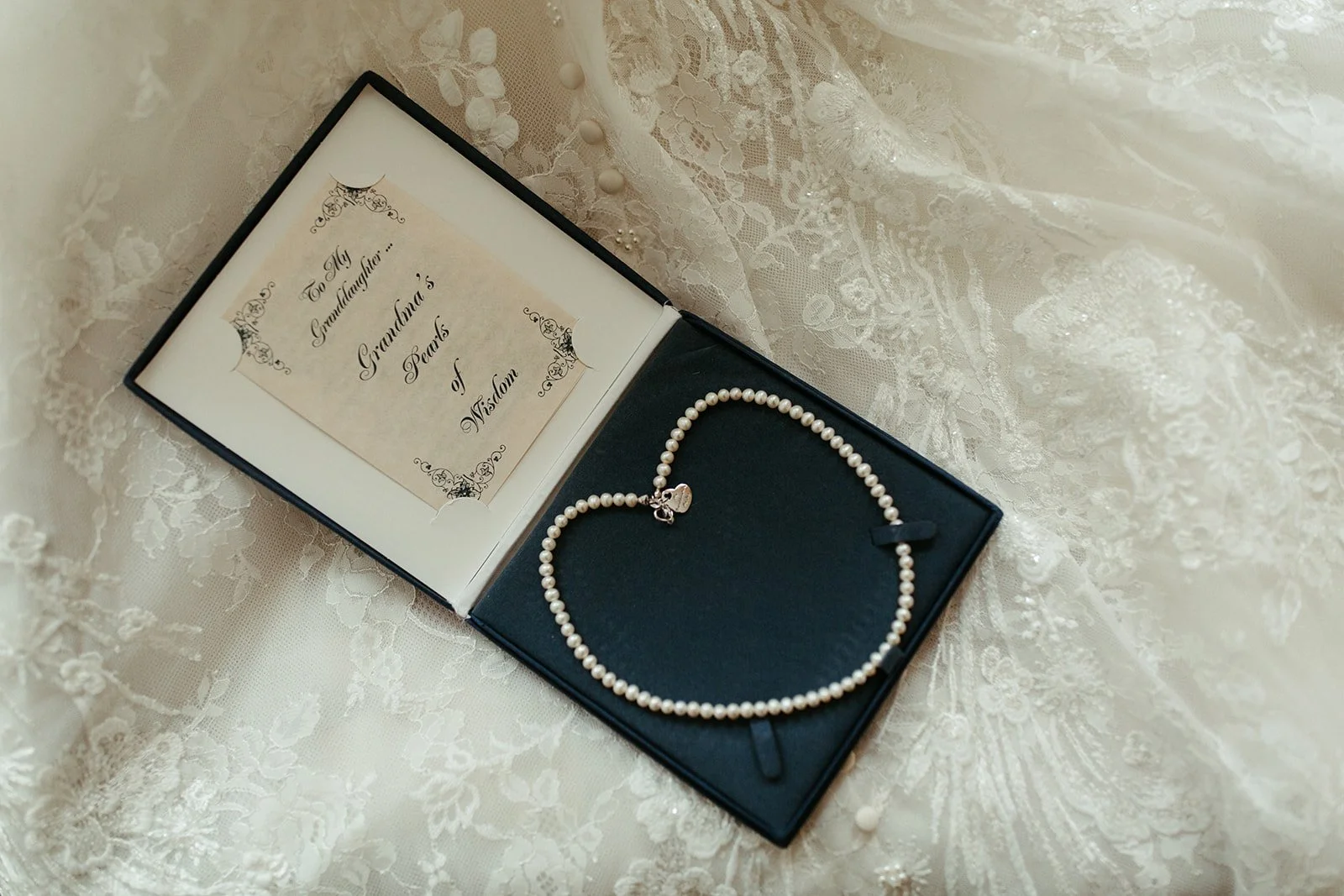 Pearl necklace and vow book with calligraphy styling on lace wedding dress fabric.
