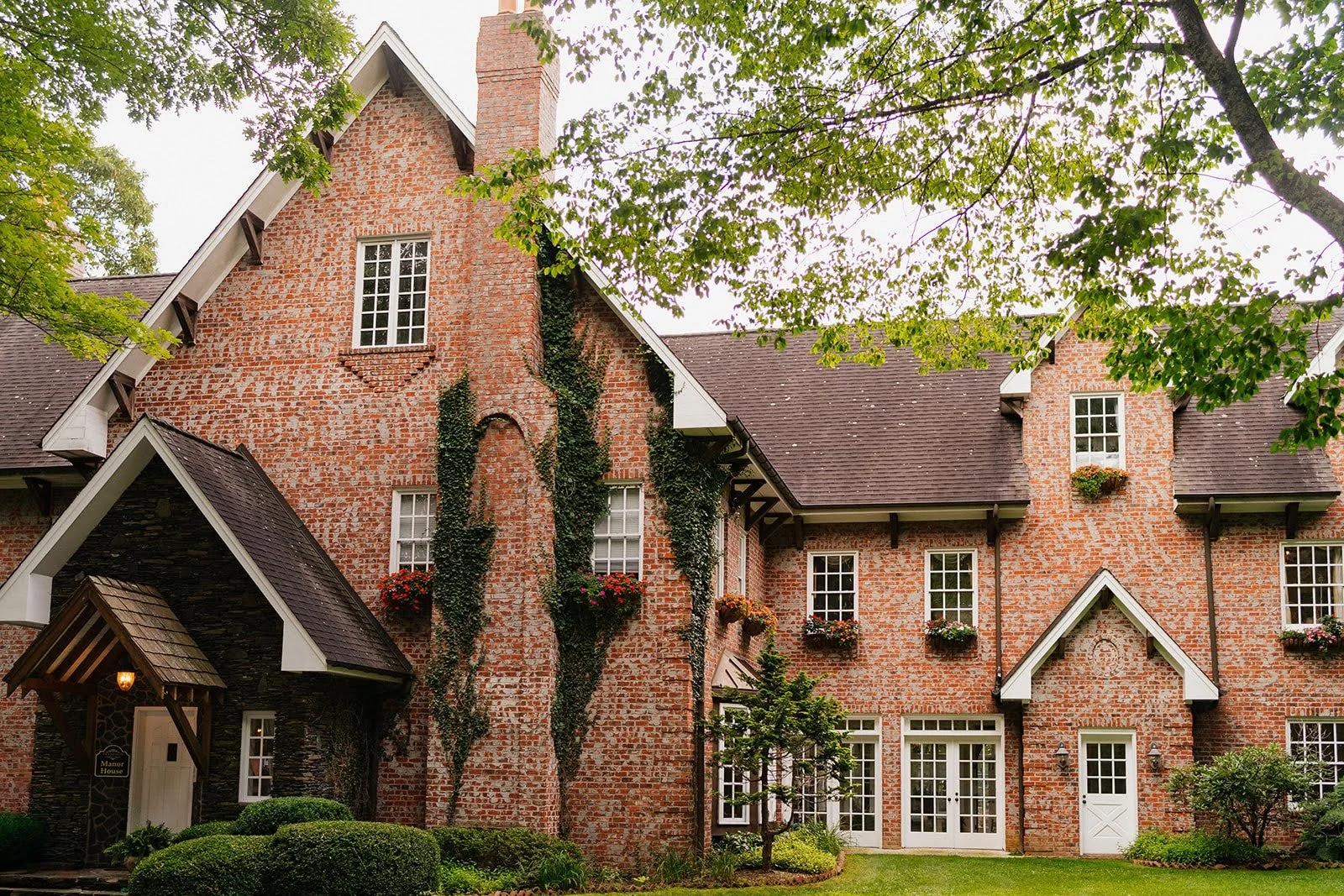 Historic brick estate wedding venue exterior with ivy, flower boxes, white trim, and surrounding trees.