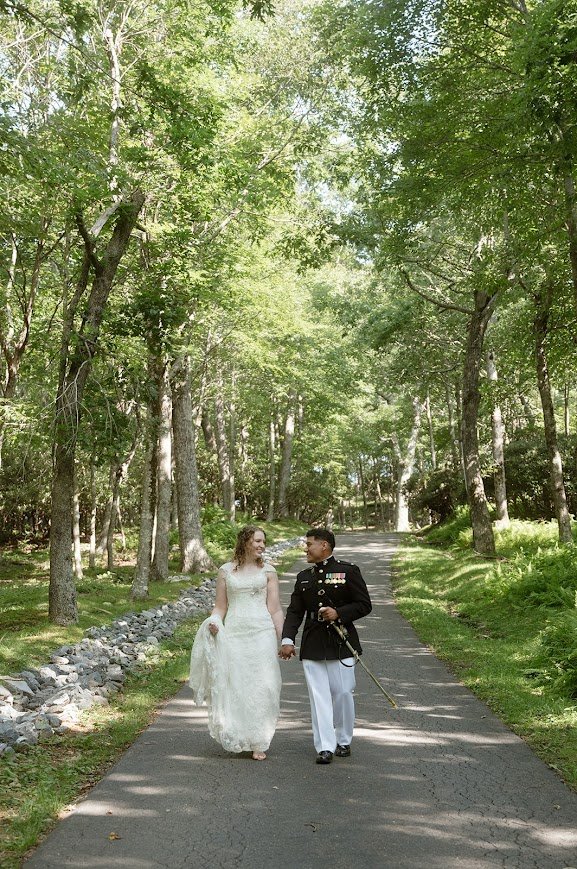 Wedding couple holding hands on a tree-lined road, groom in military dress uniform.
