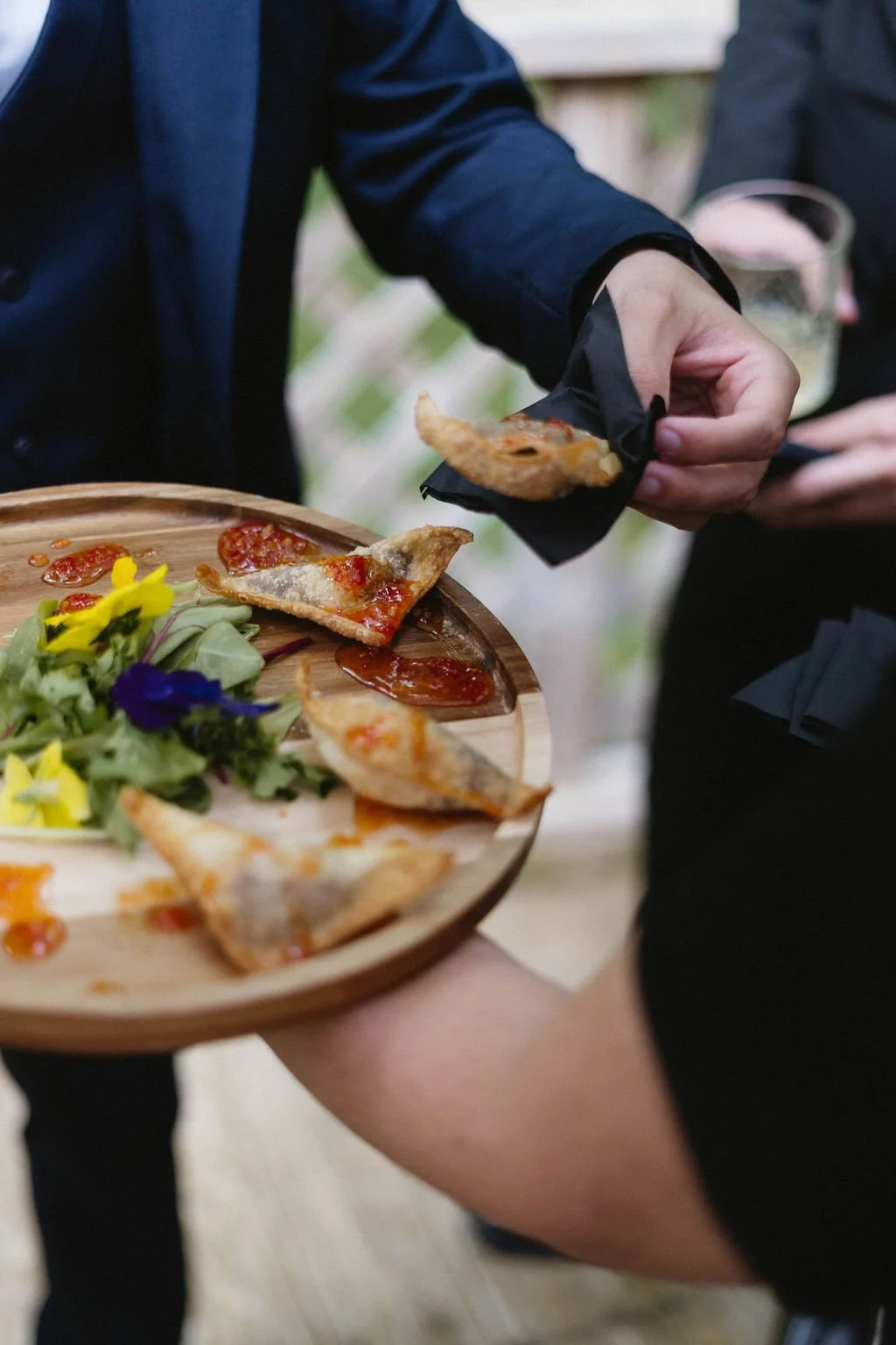 Passed wedding appetizers served on a wooden tray with sweet chili sauce and colorful edible flowers.