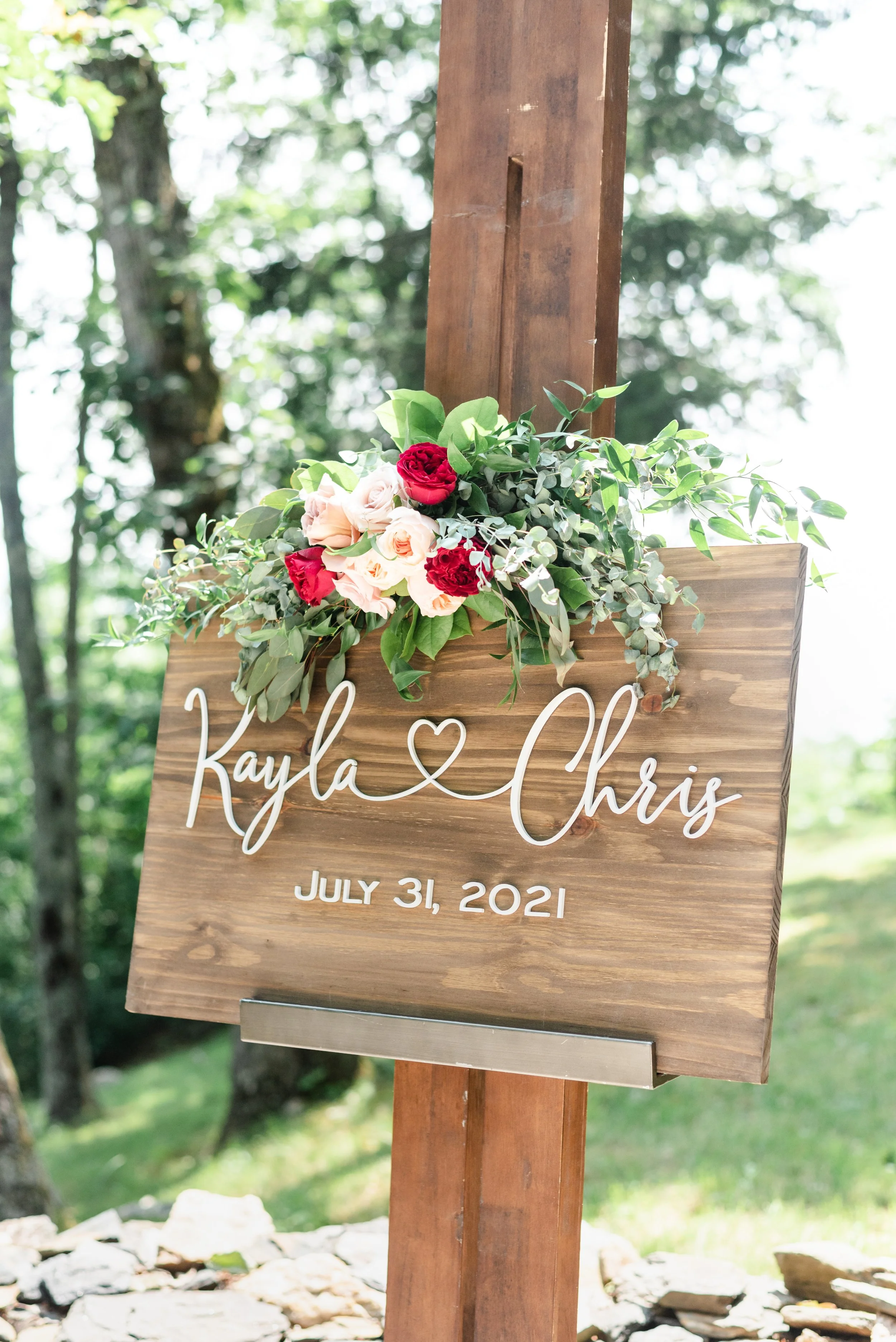 Custom wooden welcome sign reading Kayla and Chris with floral arrangement and wedding date.