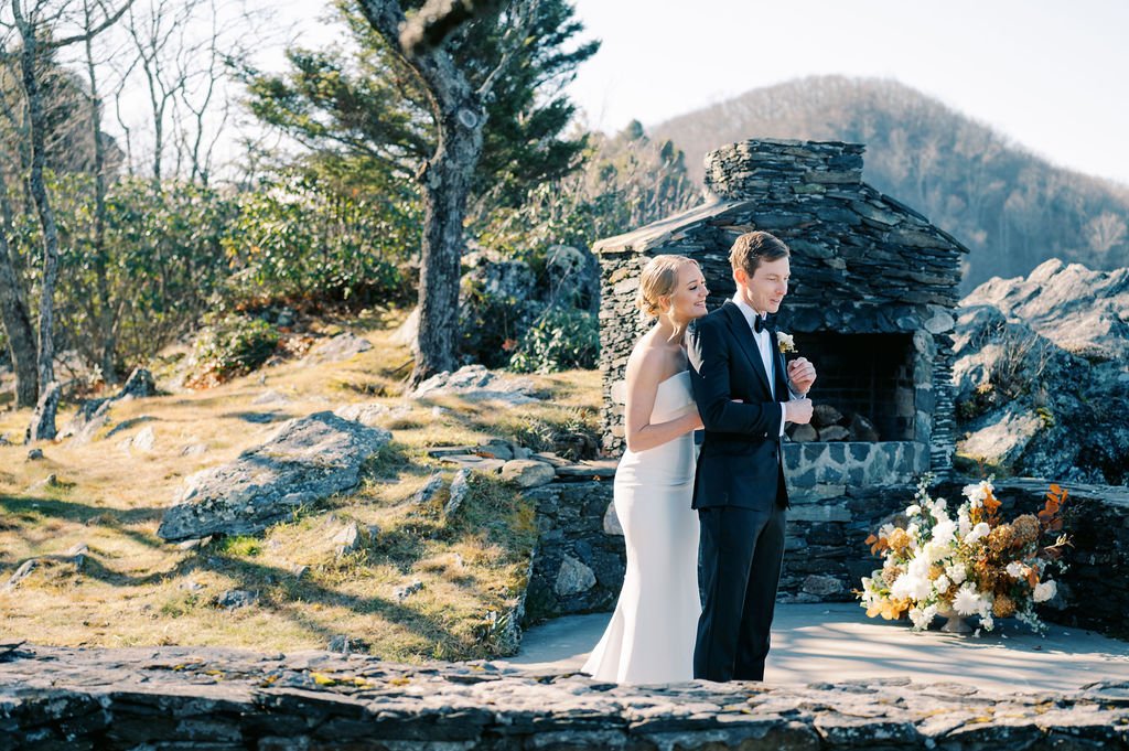 Wedding couple portrait near a stone fireplace with mountain views.