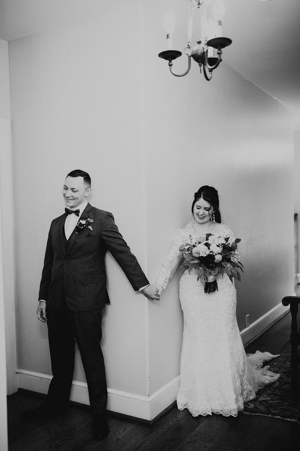 Black and white photo of the couple holding hands around a corner during a first look.