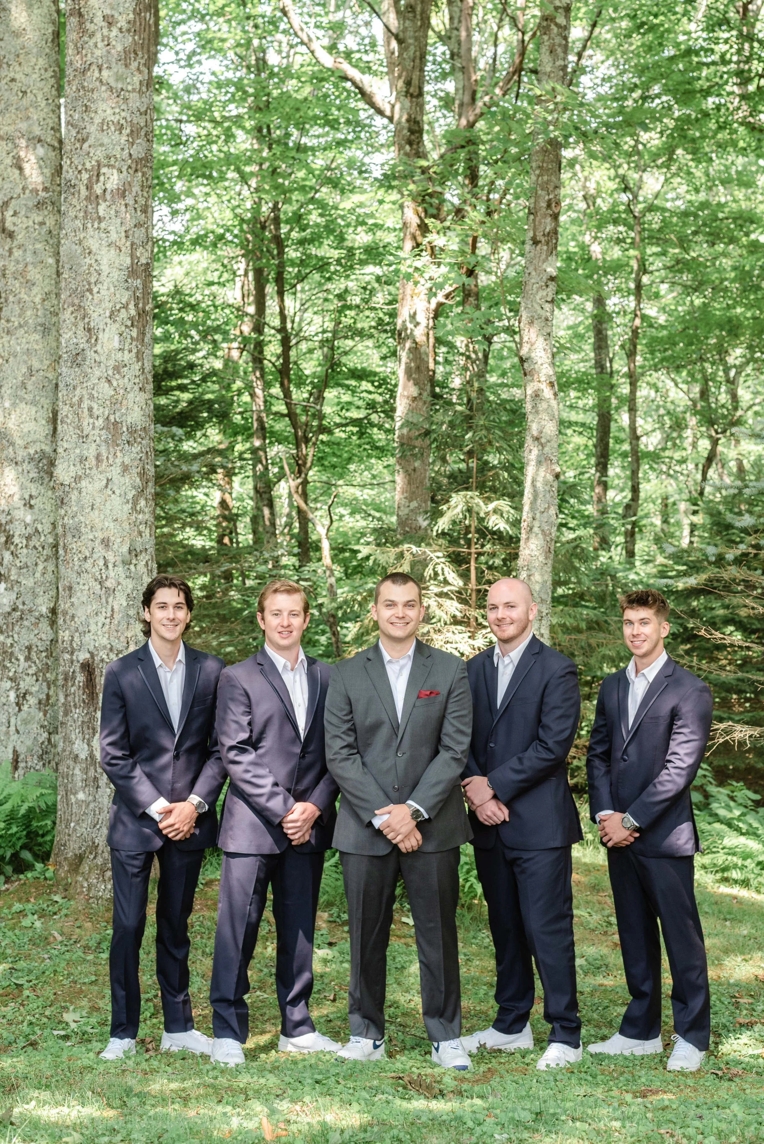 Groom and groomsmen posing in a forest wearing dark suits.