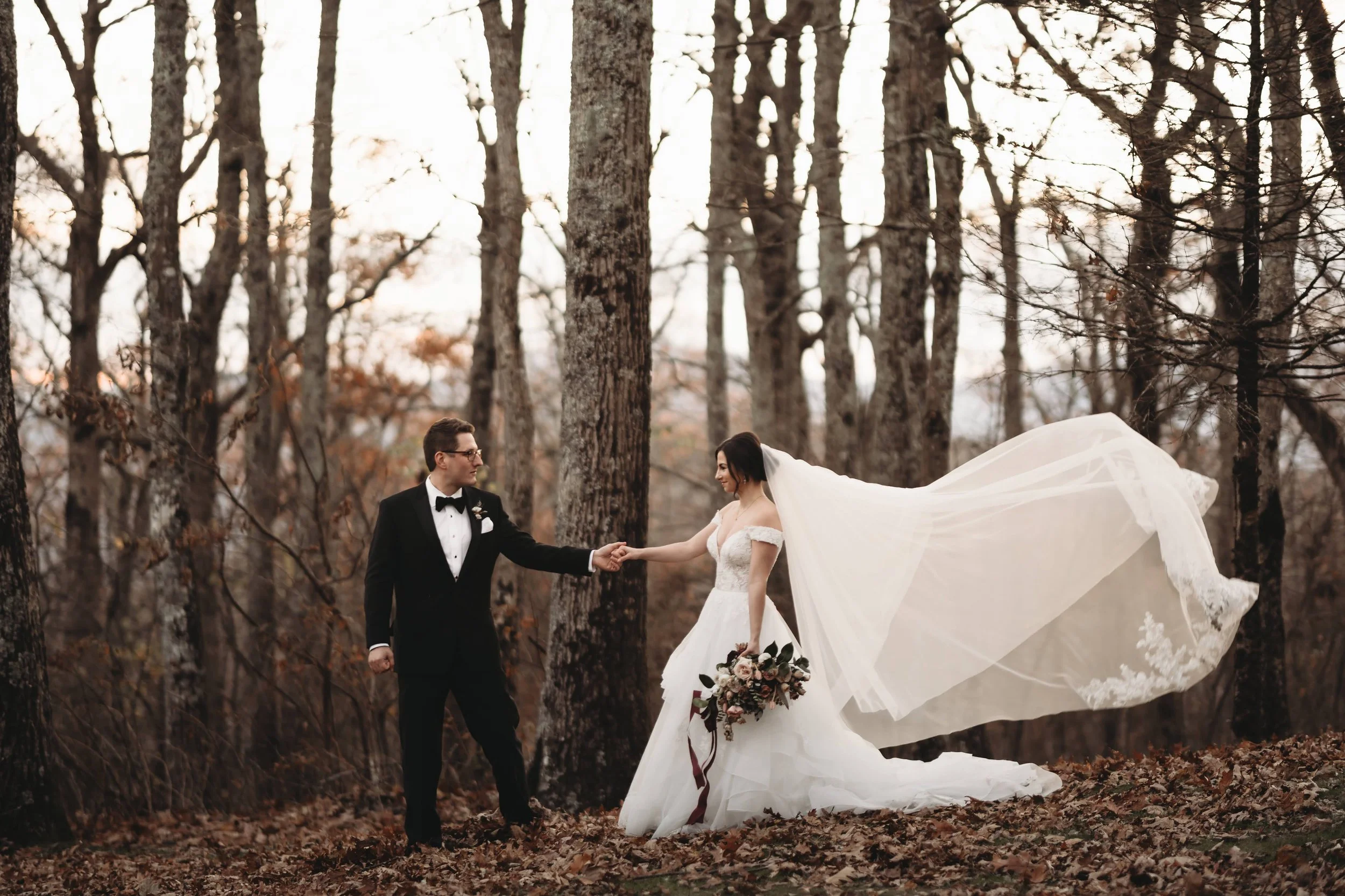 Bride and groom holding hands in the forest with the bride’s veil blowing in the wind.