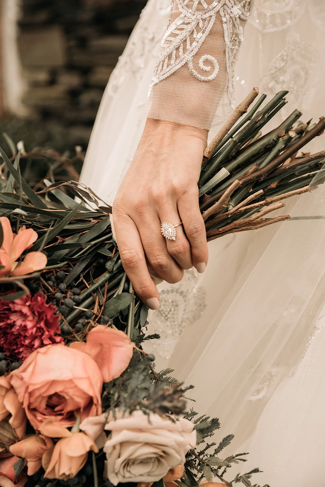 Bride holding a moody floral bouquet with her engagement ring visible against lace wedding dress details.