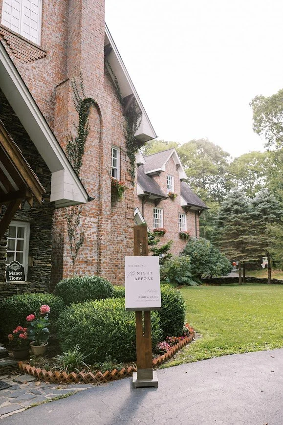 Brick manor house exterior with lawn and event sign for an outdoor wedding celebration.