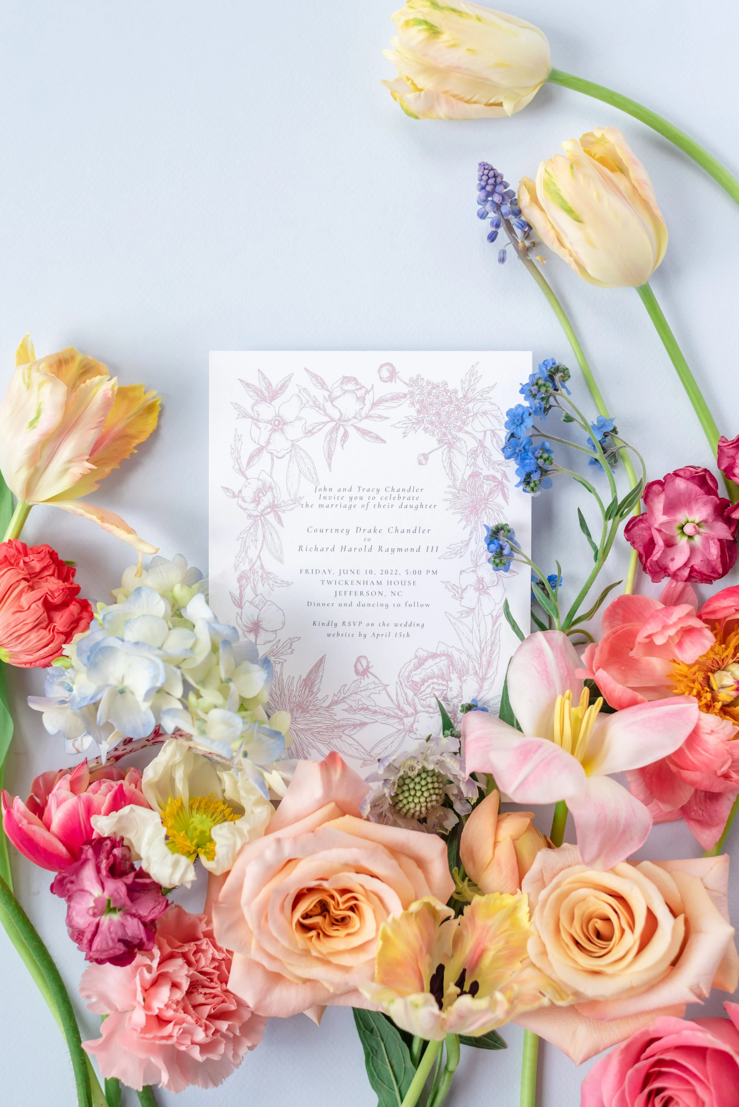 Pastel floral wedding invitation suite surrounded by colorful flowers and soft blue details.