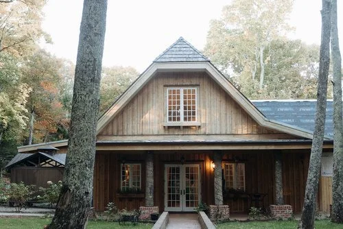 Exterior view of Twickenham House, a rustic wooden building with a distinctive roofline and a welcoming front porch with white double doors.