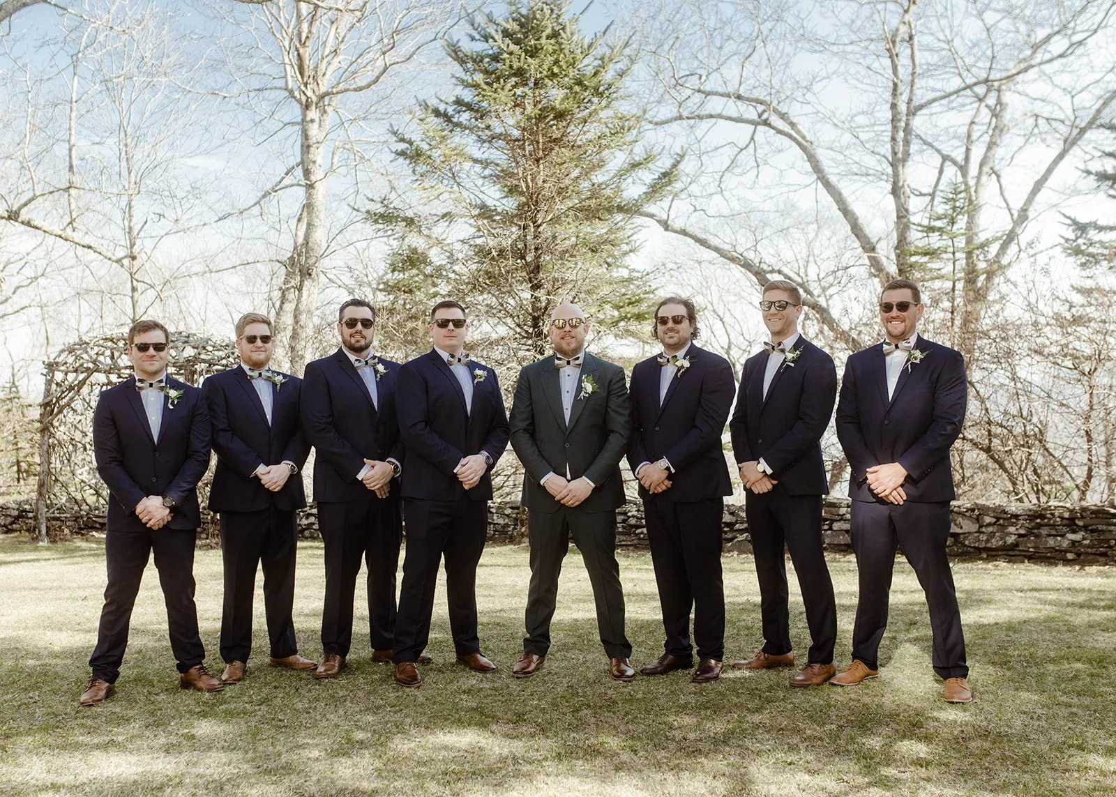 Groom and groomsmen in navy suits posing together outdoors before the wedding ceremony.