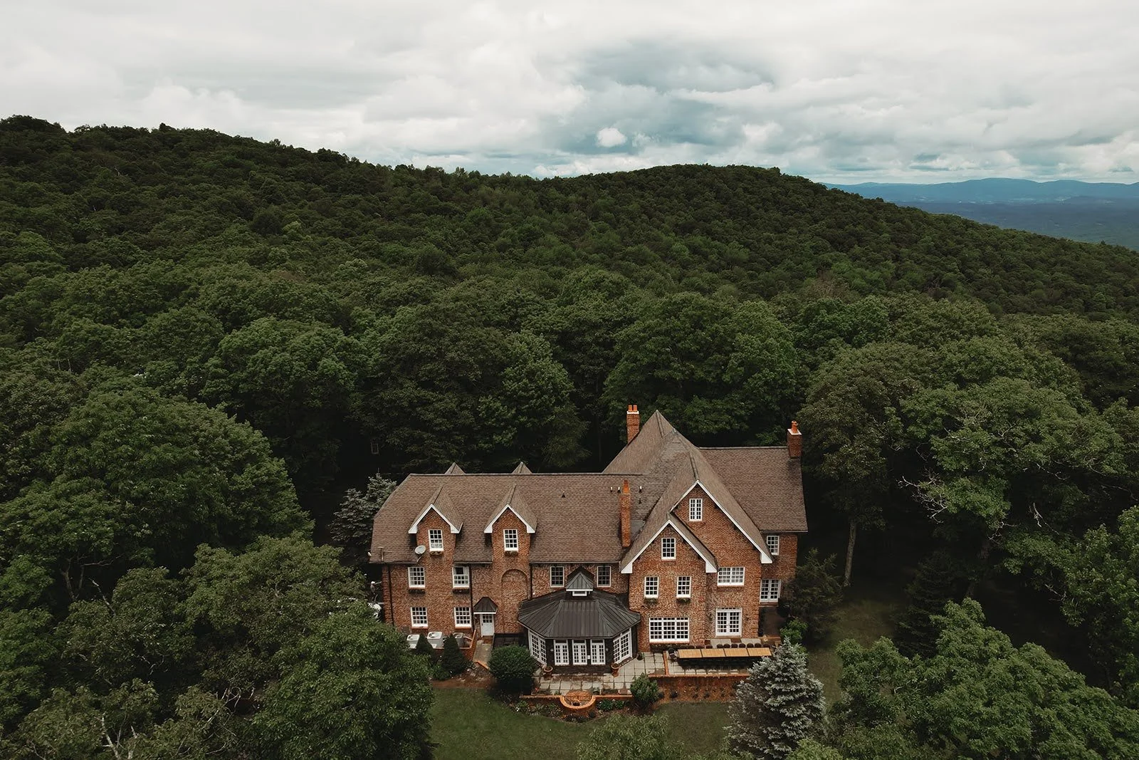 Aerial view of a brick estate wedding venue surrounded by forested mountains.