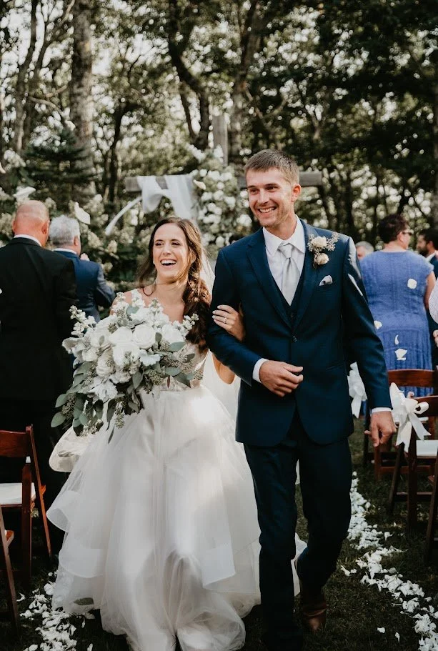 Newlyweds smiling and walking arm in arm down the aisle after their outdoor wedding ceremony.