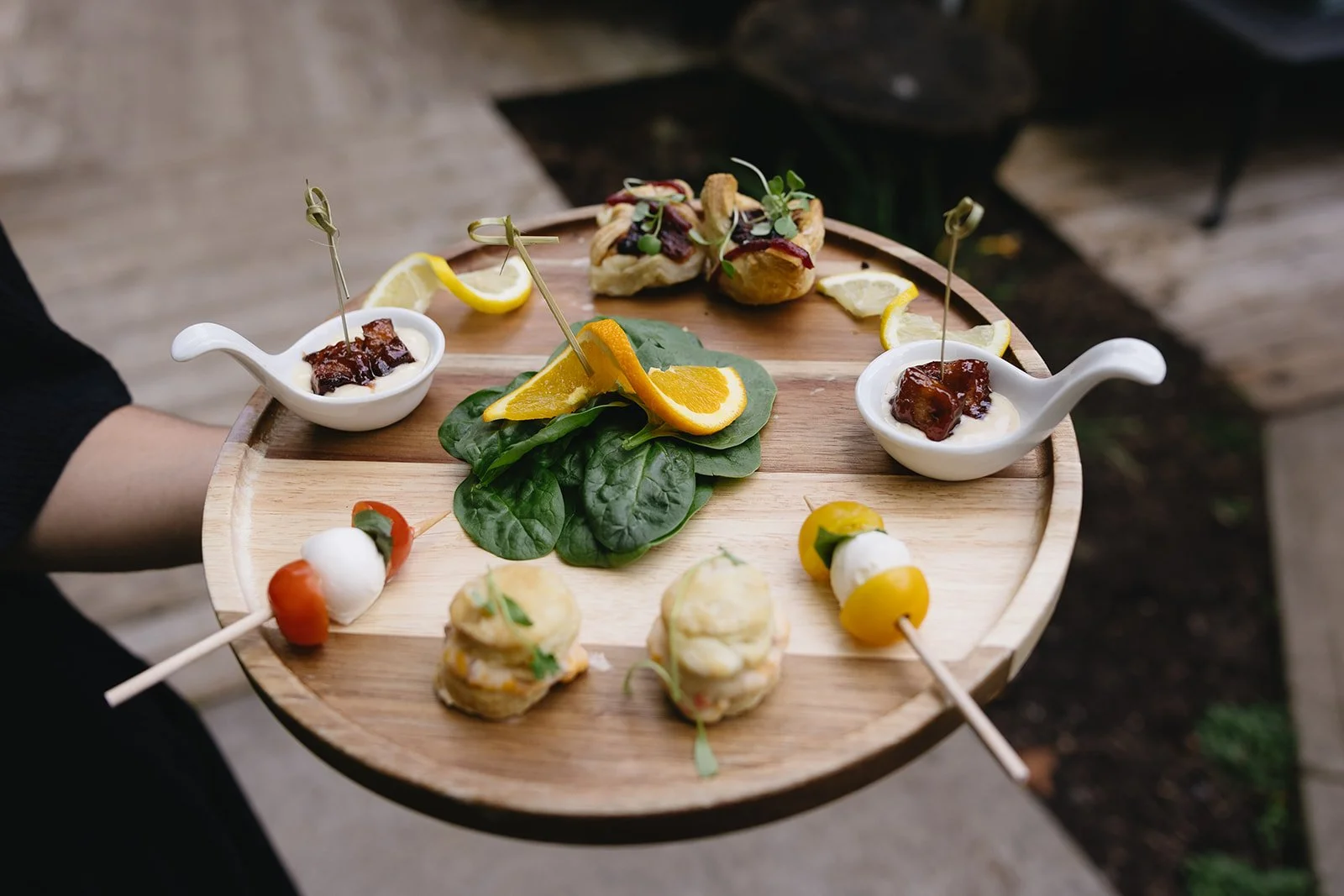 Passed wedding cocktail hour appetizers on a wooden serving tray with citrus garnish.