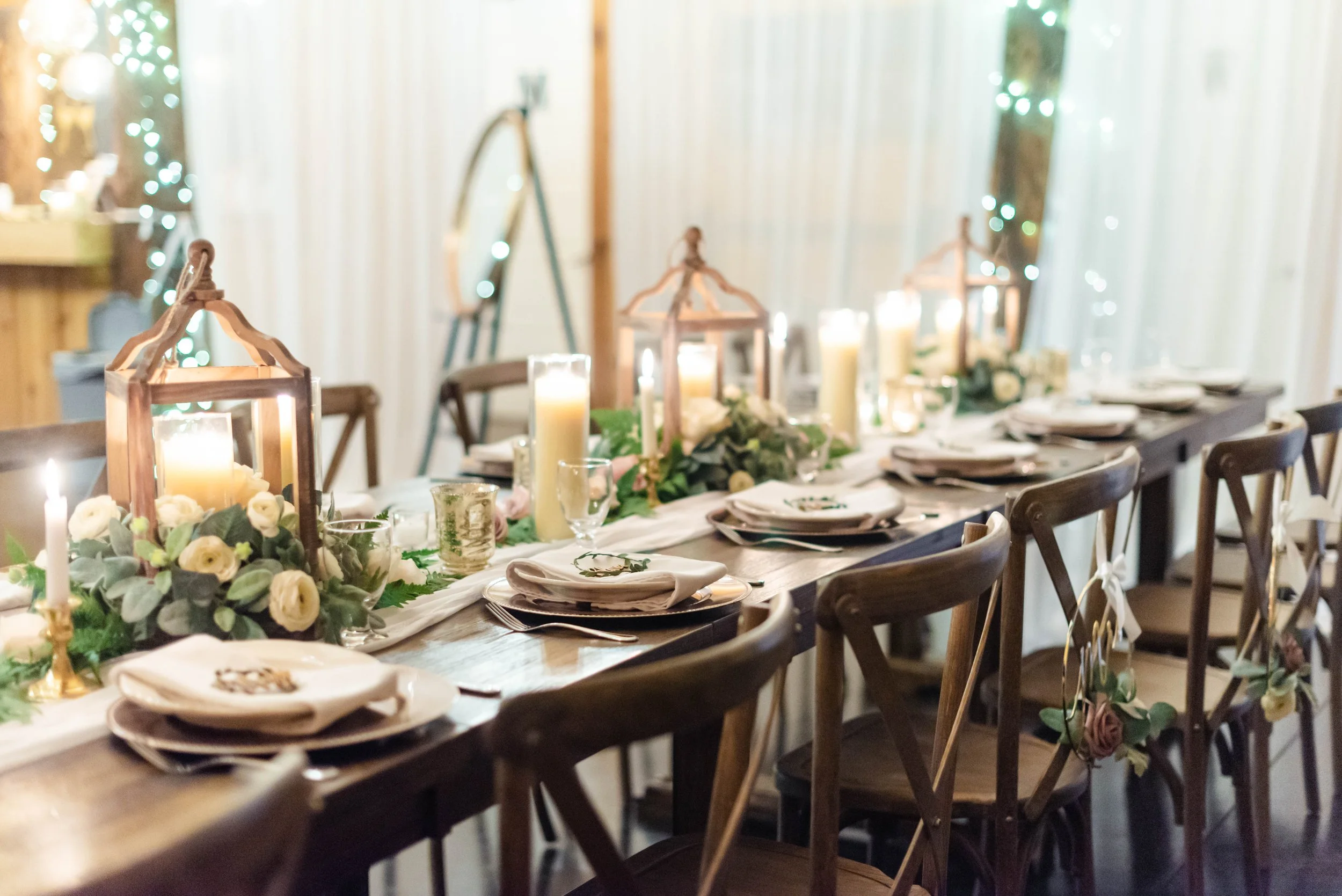 Long rustic reception table with lantern centerpieces, candles, and greenery garland
