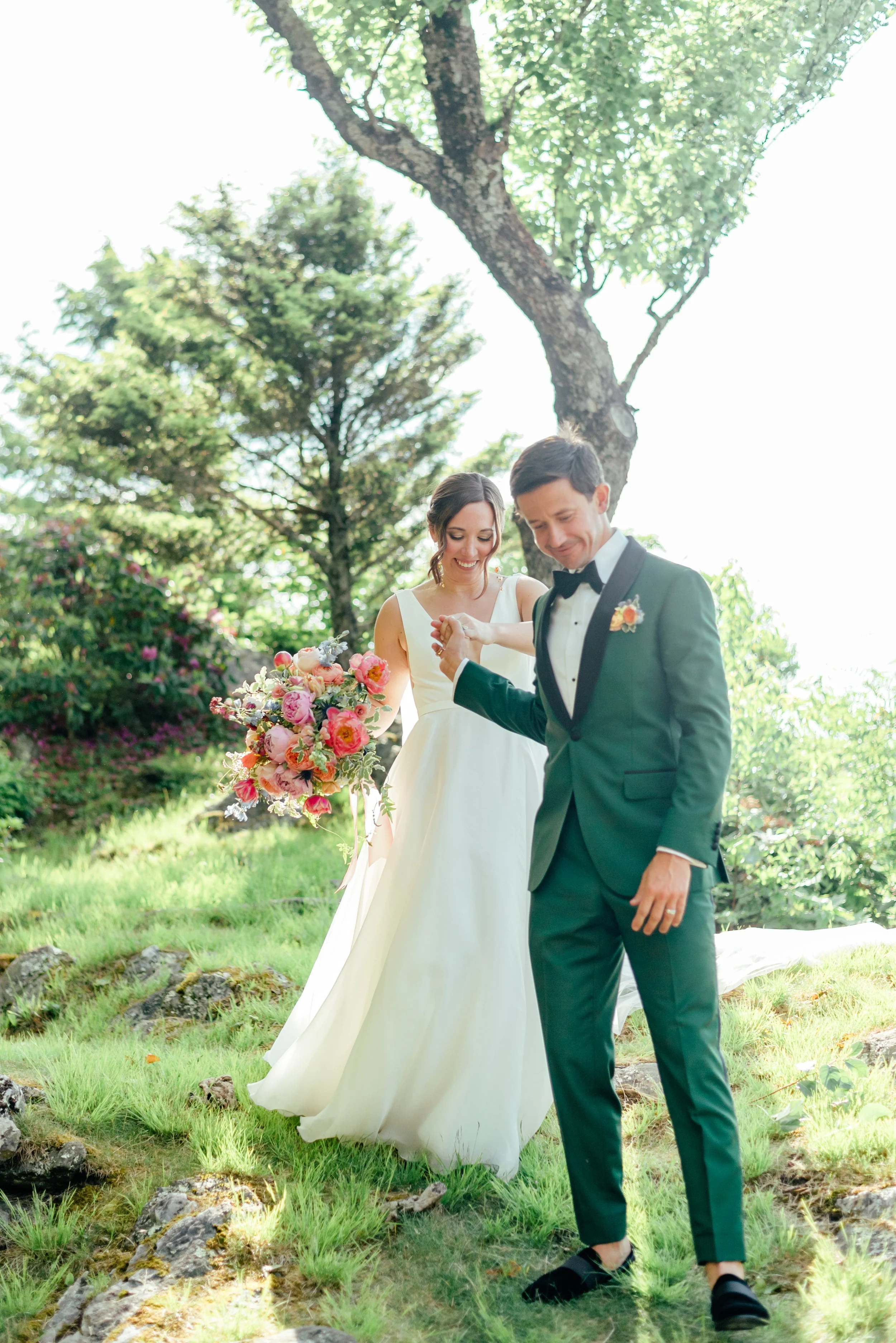 Bride and groom walking together through a garden with bright florals and a green groom suit.