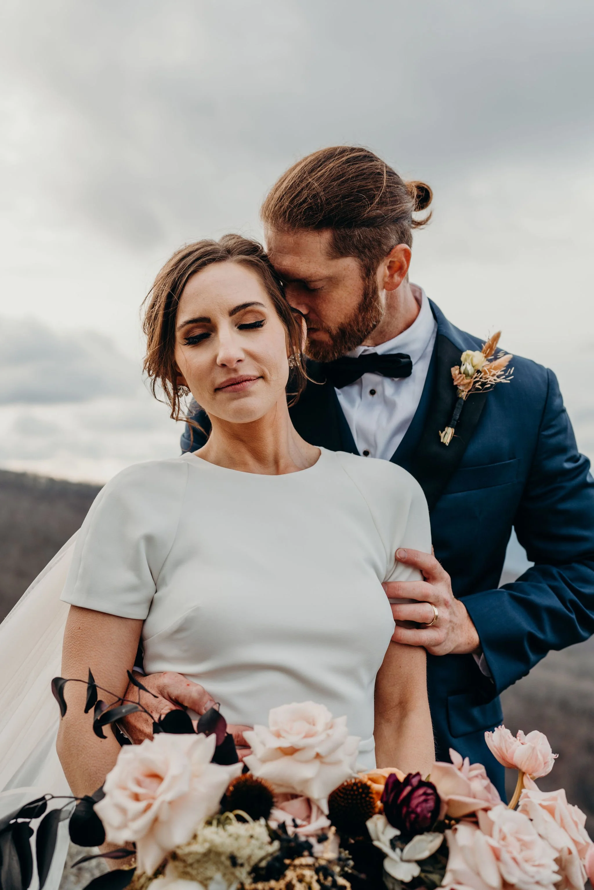 Romantic closeup of the couple laughing together at a mountain overlook, groom in a blue suit.