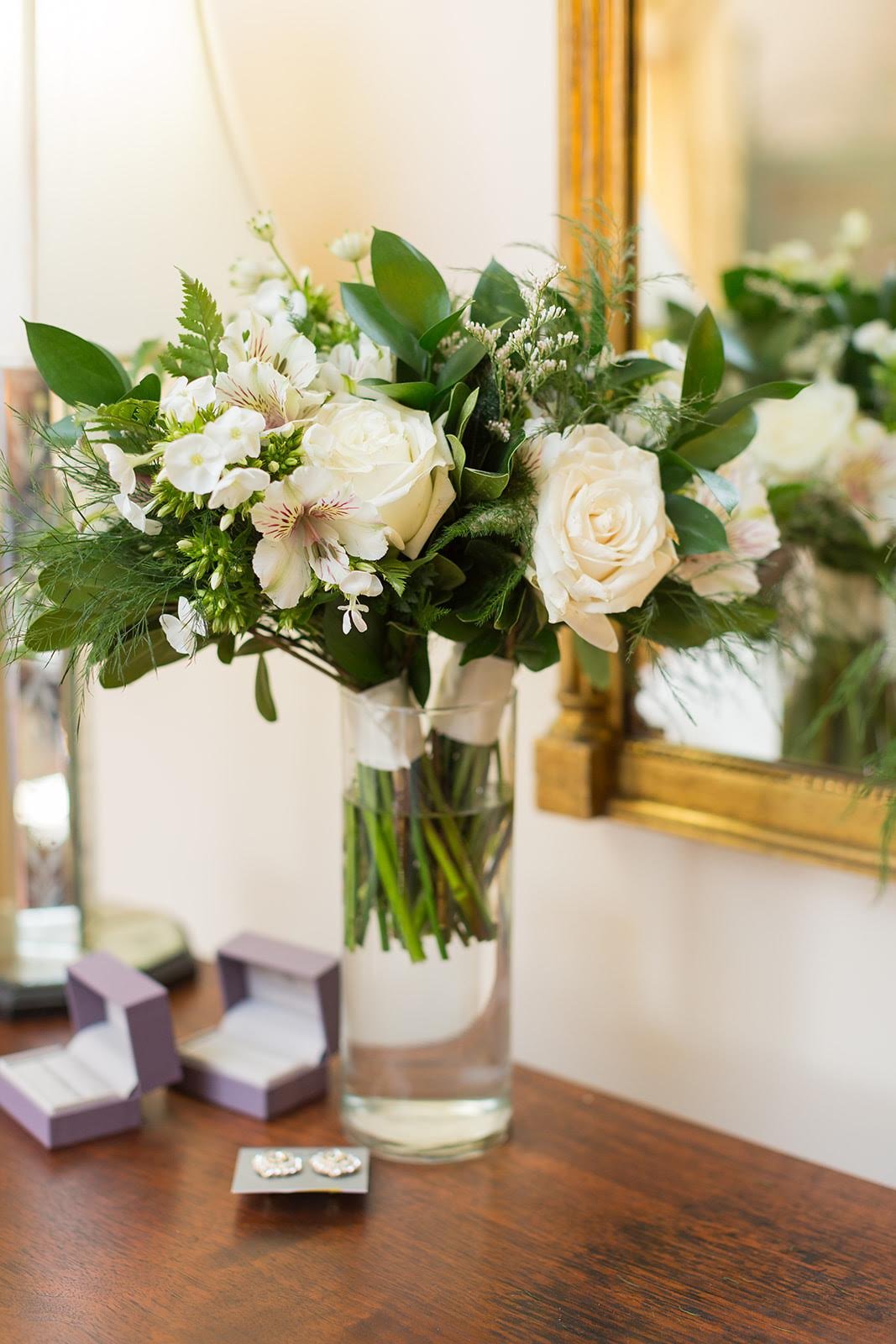 White rose bouquet in a glass vase on a table during wedding getting-ready details.