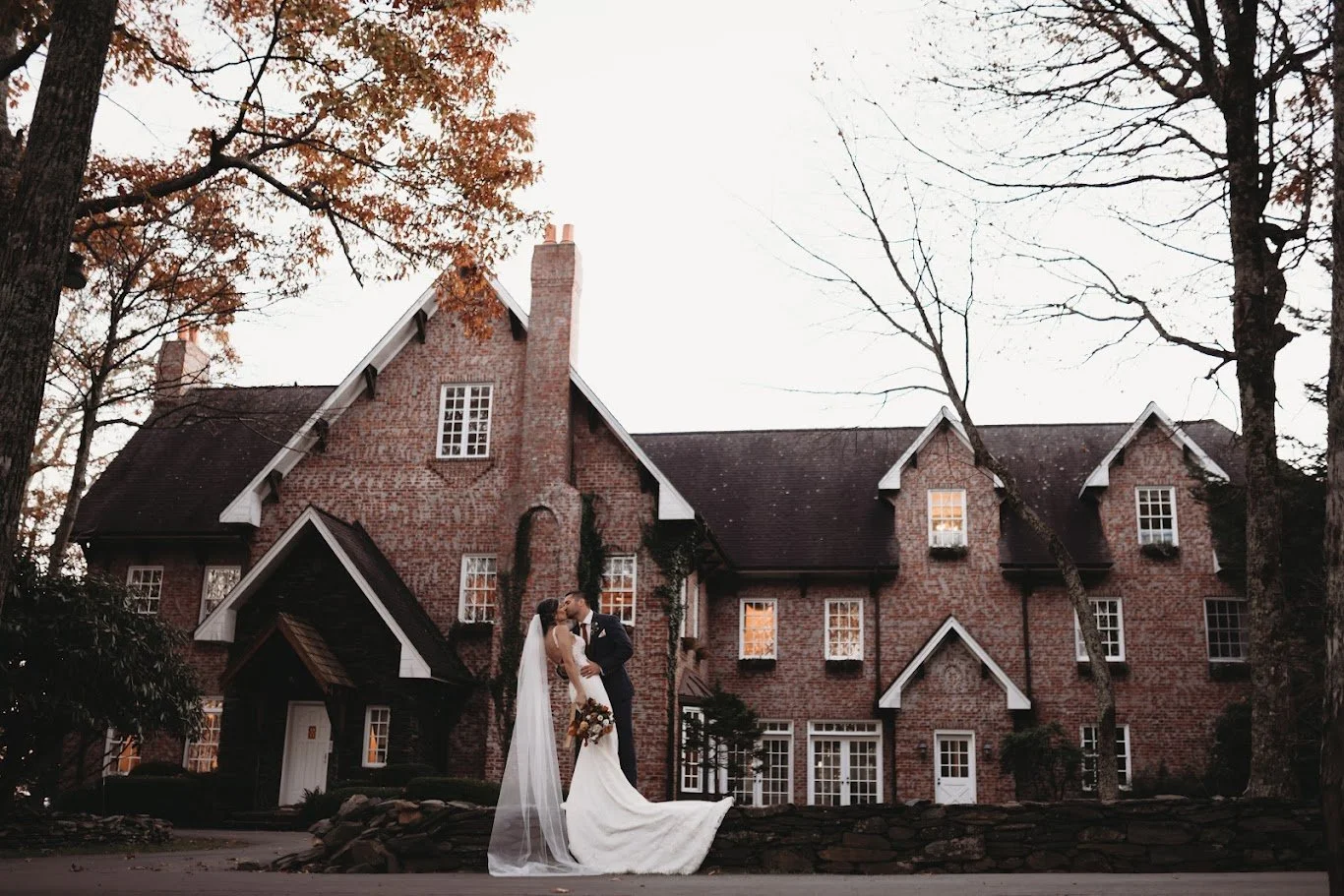 Bride and groom kissing in front of a brick estate wedding venue with gables and ivy