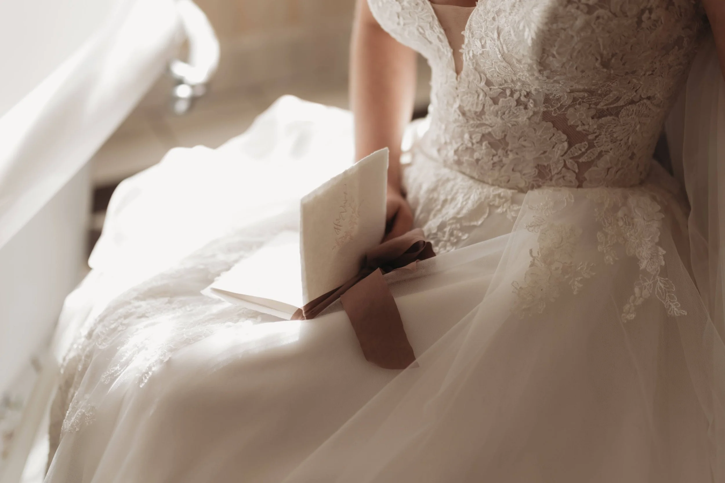 Closeup of the bride’s lace bodice as she holds a small vow book or letter in her lap.