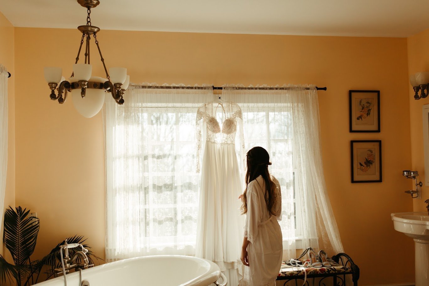 Bride standing in silhouette by a bright window before her mountain wedding ceremony.