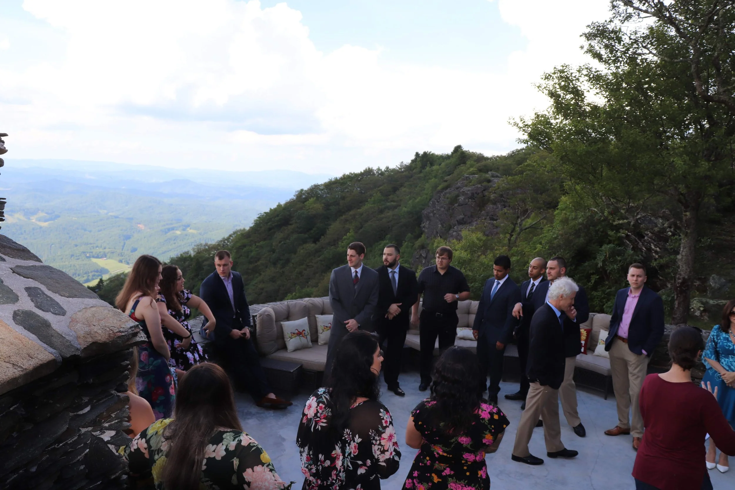 Executive retreat guests mingling during cocktail hour on a mountain terrace with stone walls, lounge seating, and valley views.