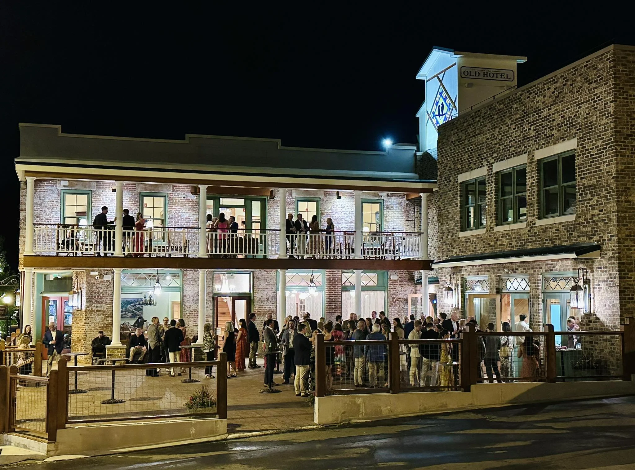 Nighttime scene with a crowd gathered outside the hotel and people standing along the balcony railings.