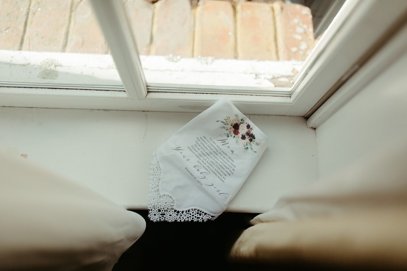 Wedding rings displayed on a light surface near a window for a simple bridal detail photo.
