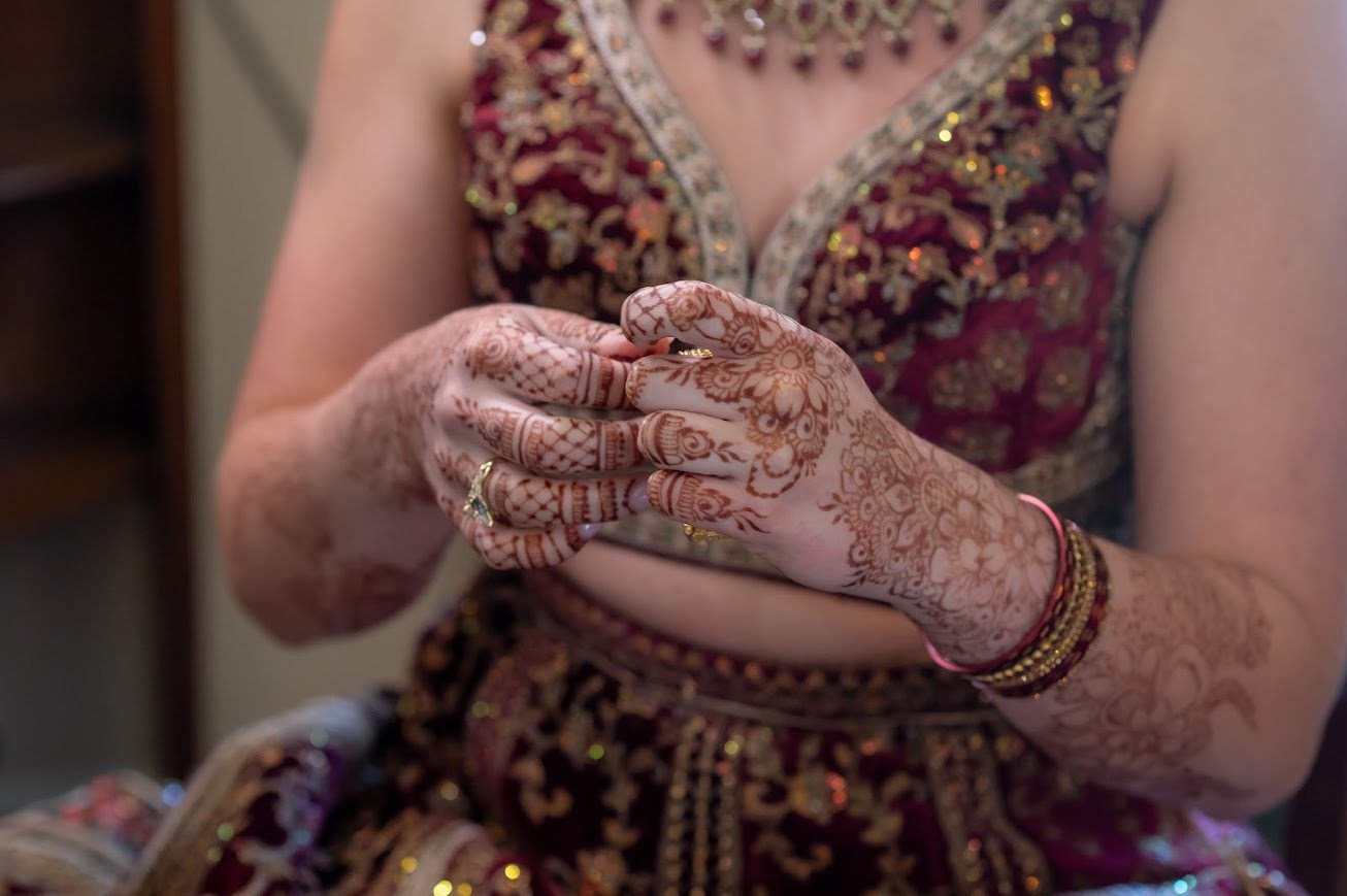 Close-up of hands with intricate mehndi (henna) and bangles during a South Asian wedding event.