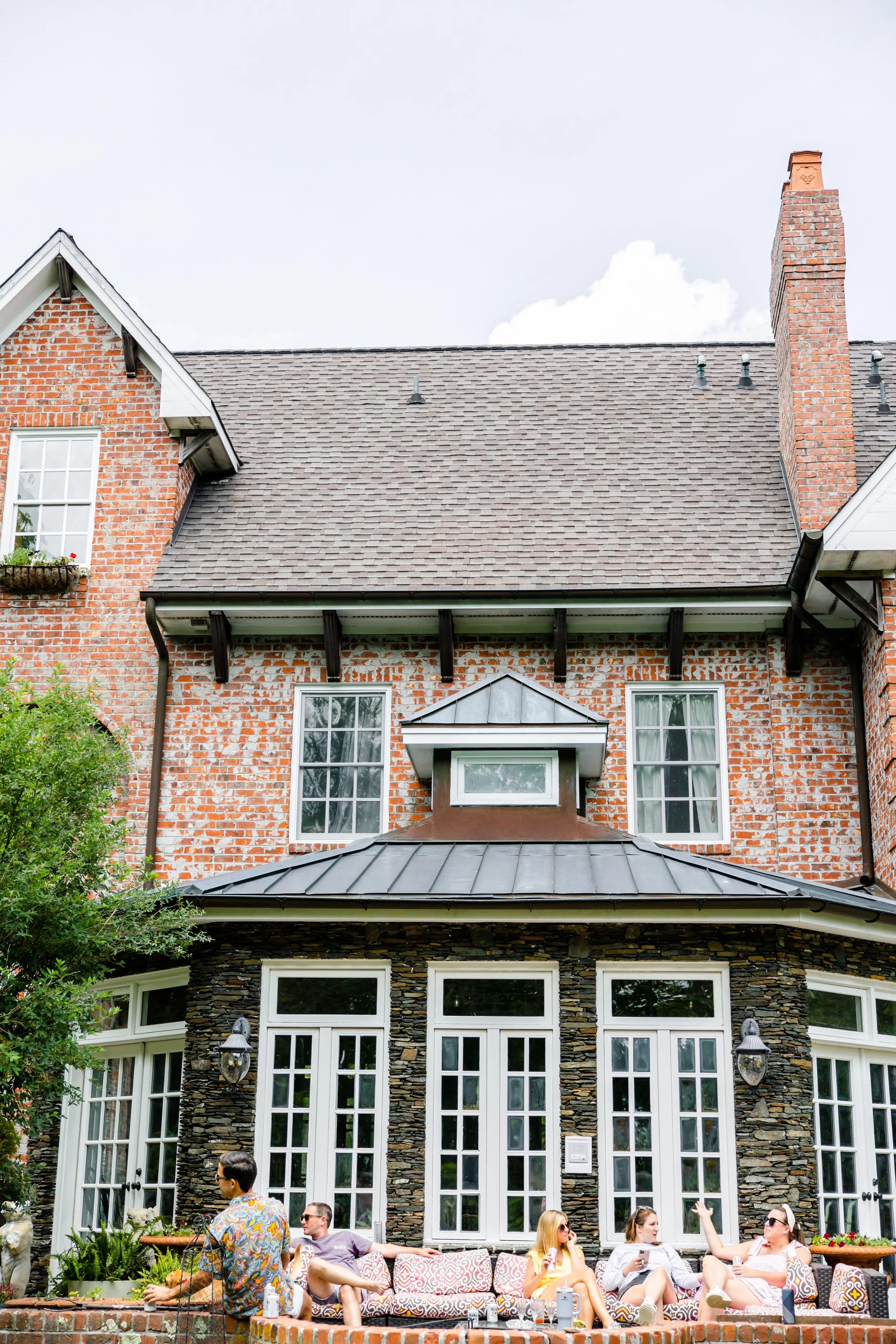 Historic brick wedding venue exterior with patio seating, white doors, and guests relaxing outside.