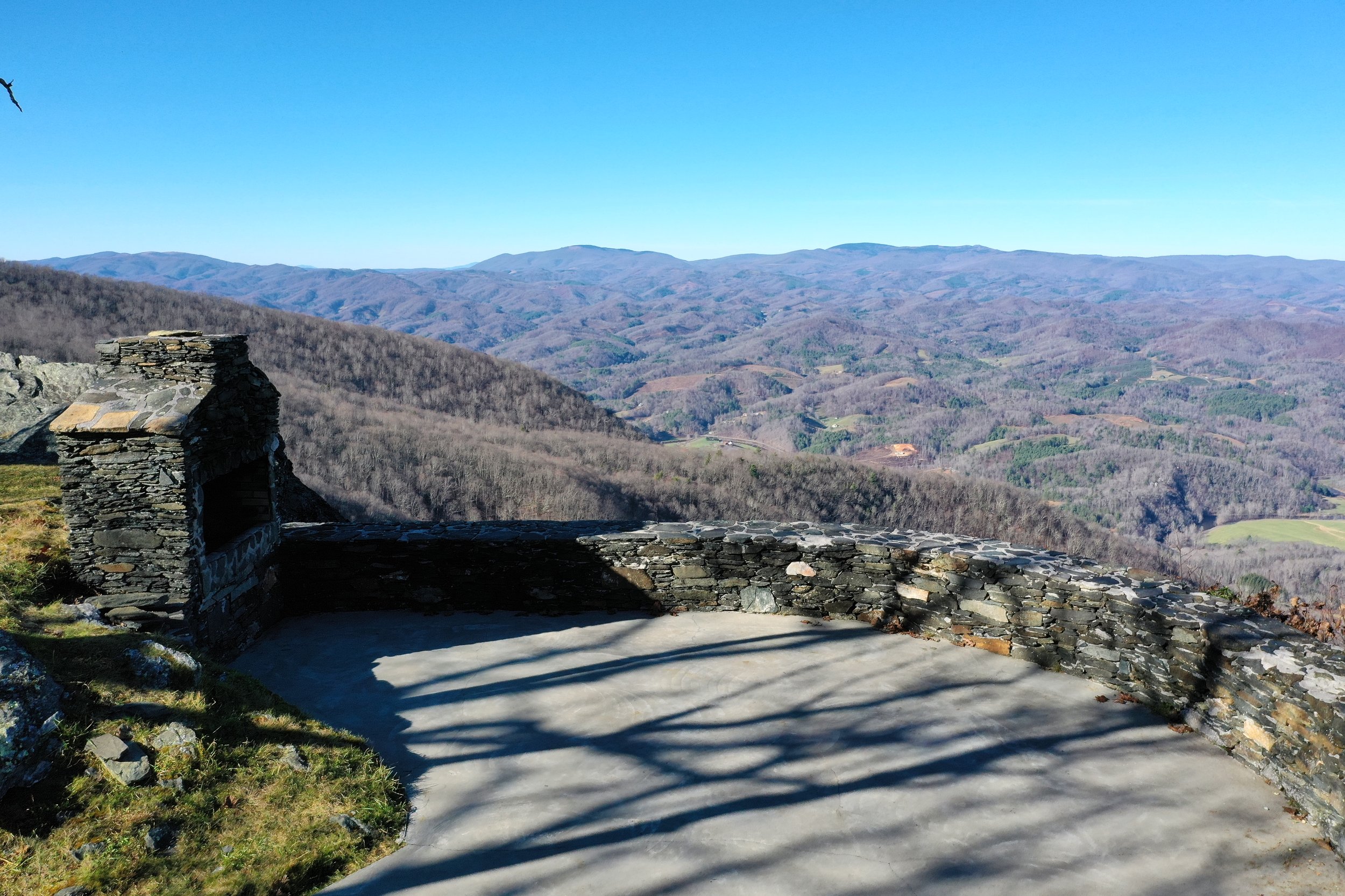 Empty stone terrace overlook with a low stone wall framing sweeping mountain views under a clear blue sky
