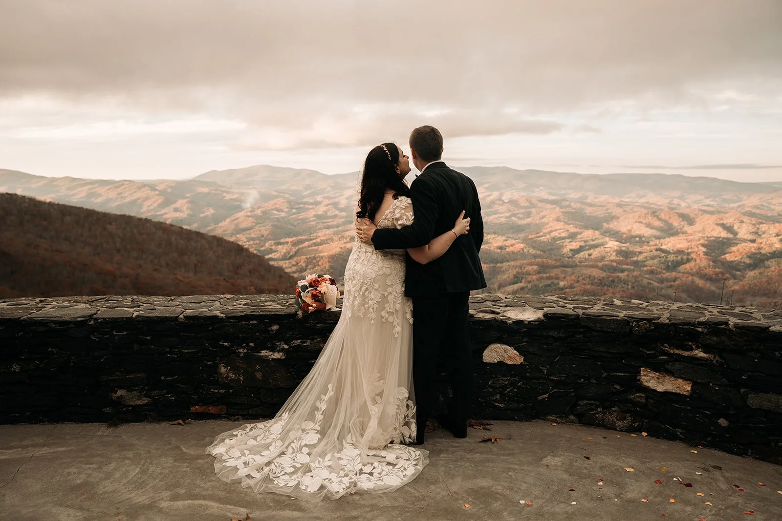 Bride and groom seen from behind on a stone terrace overlooking mountains and valleys